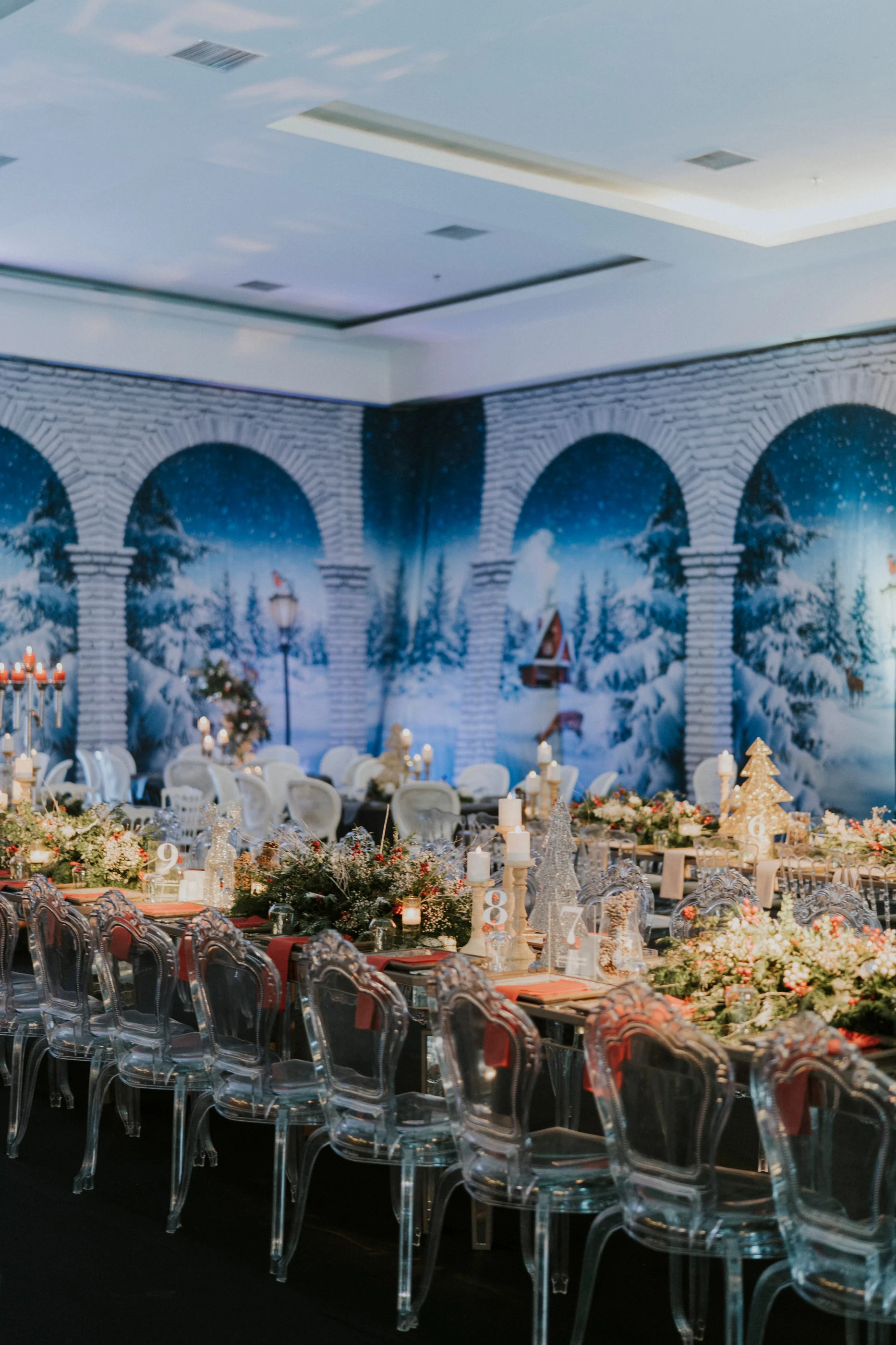 Long table dressed with greenery and candles along a wall of snowy landscape arches