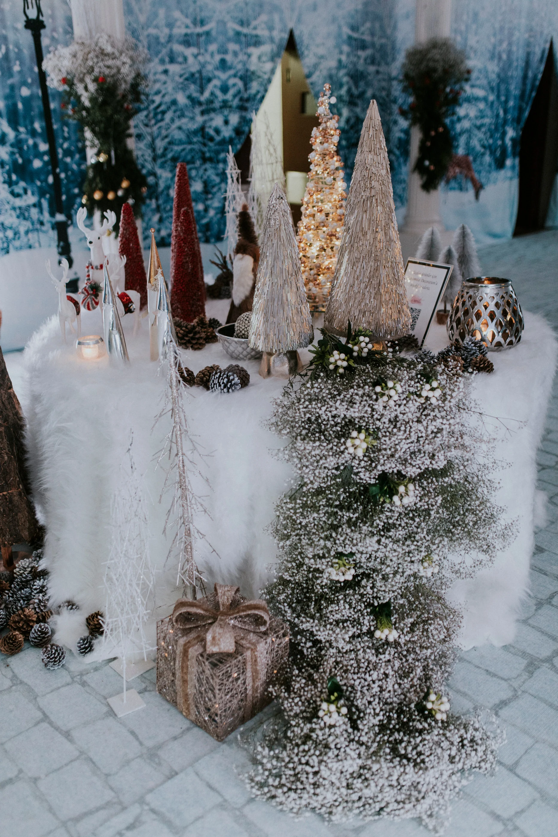 Red and silver cone trees and a gift box on a white fur-covered table