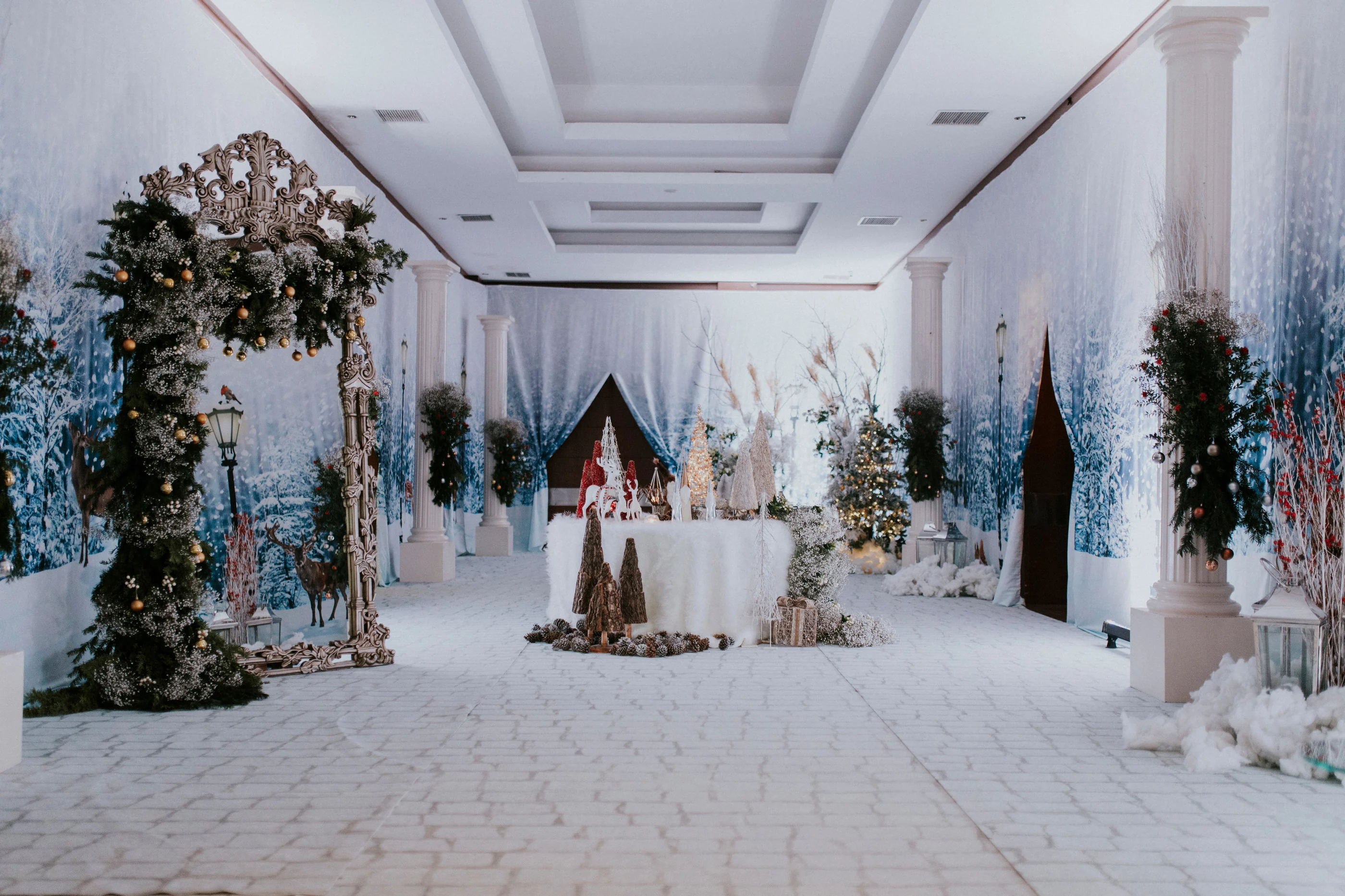 Greenery-covered arch and a round table in a white hall with snowy tree backdrops