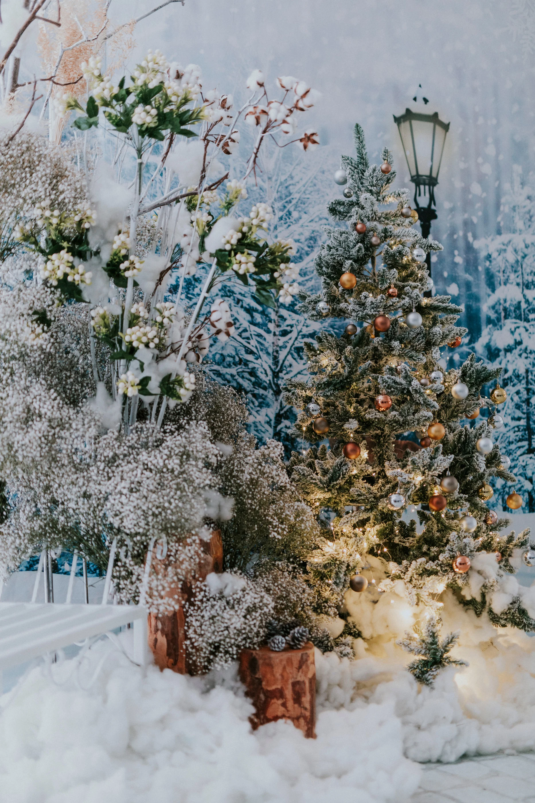 Decorated Christmas tree, street lamp and white flowers on cotton snow
