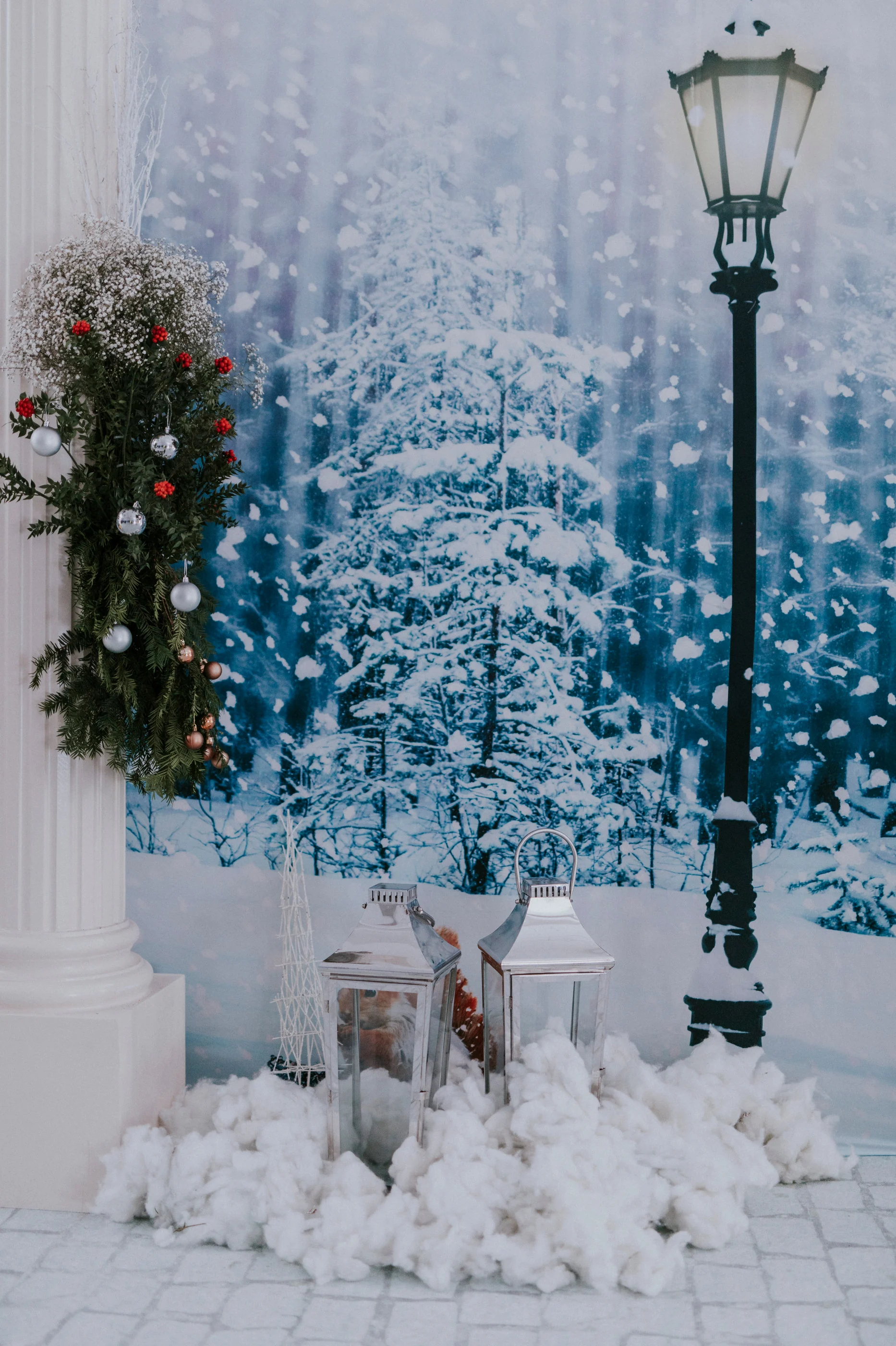 Street lamp, lanterns and cotton snow piles in front of a snowy forest backdrop