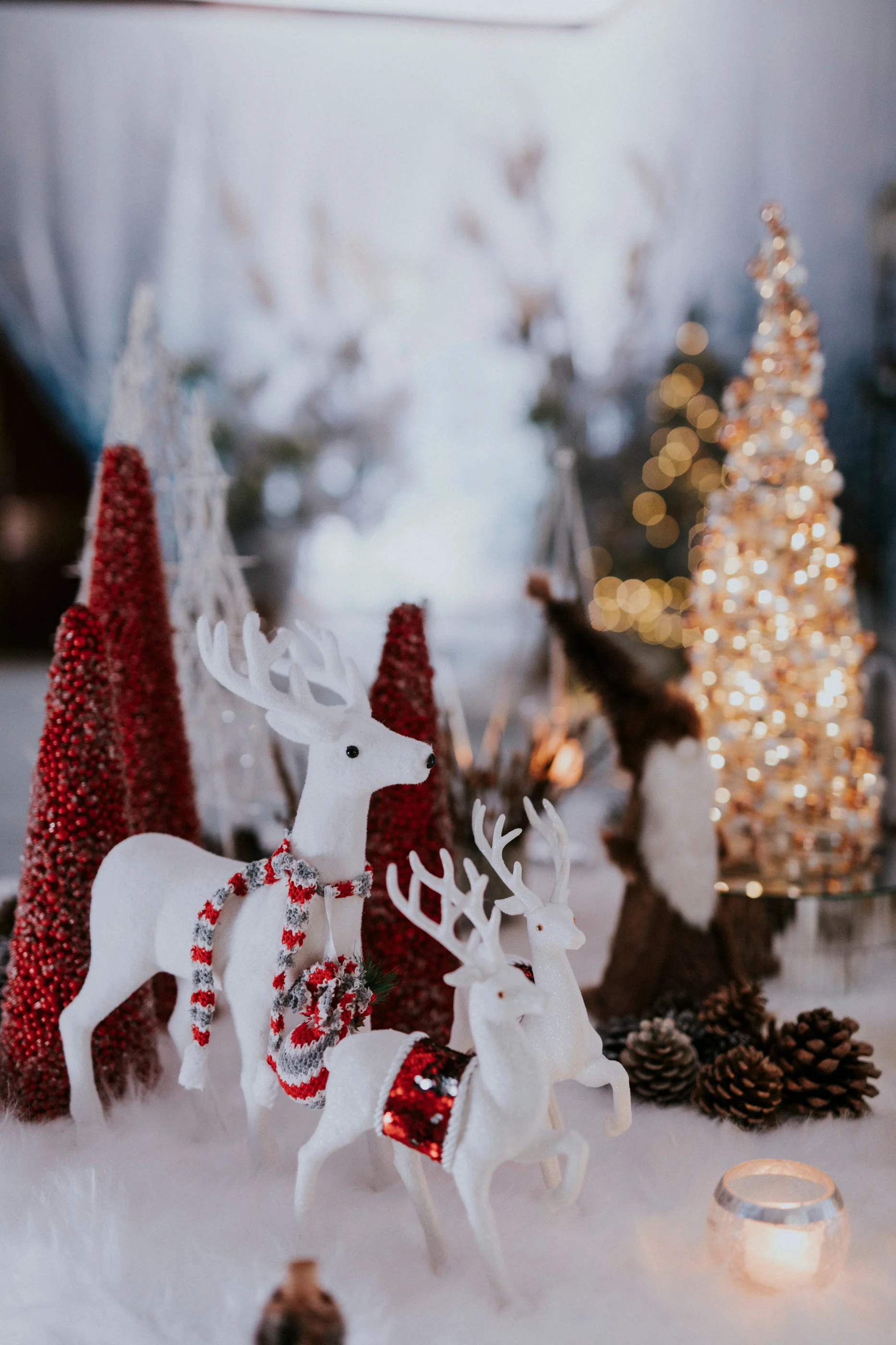 White reindeer figures among red cone trees and pine cones