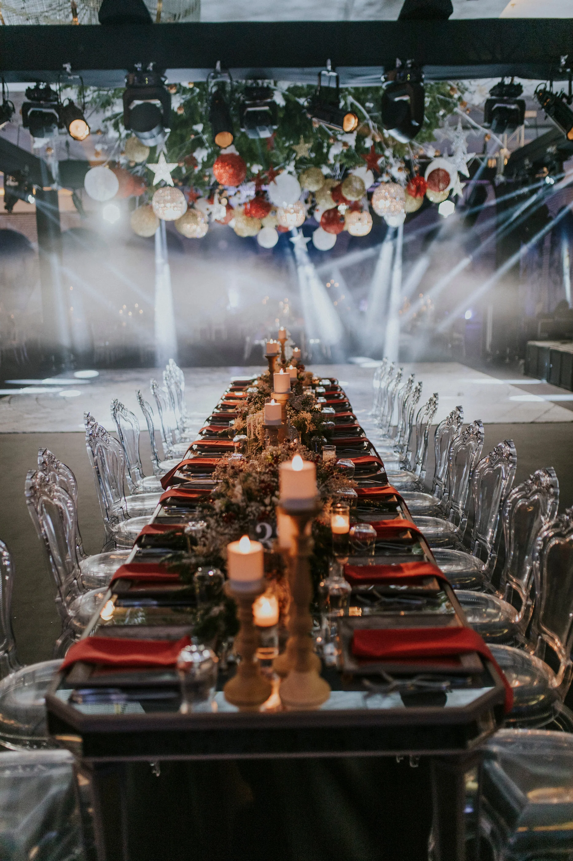 Single long table with gold candlesticks and red napkins beneath hanging ornaments