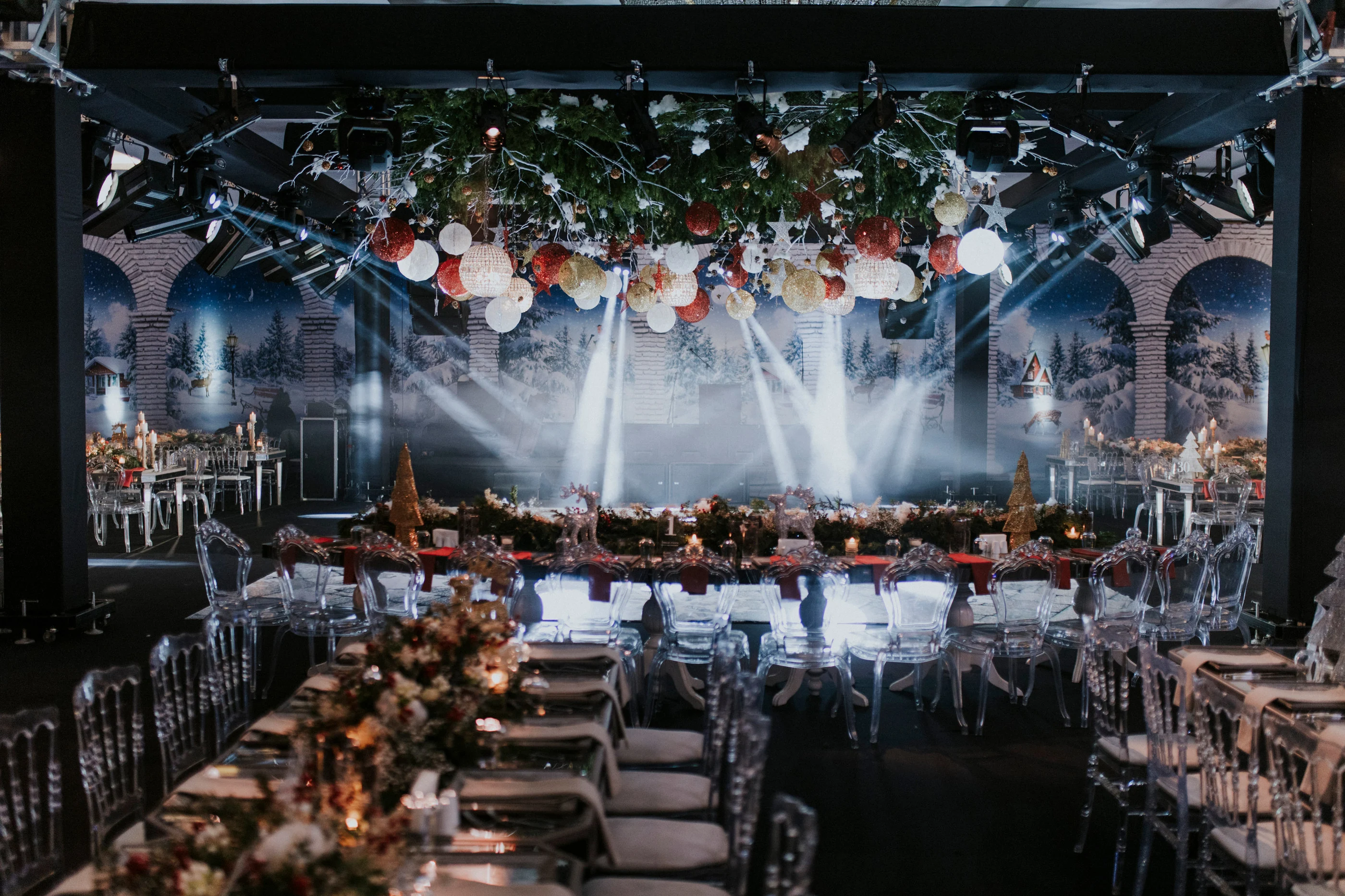 Ceiling hung with red and gold baubles above tables before an arched winter backdrop