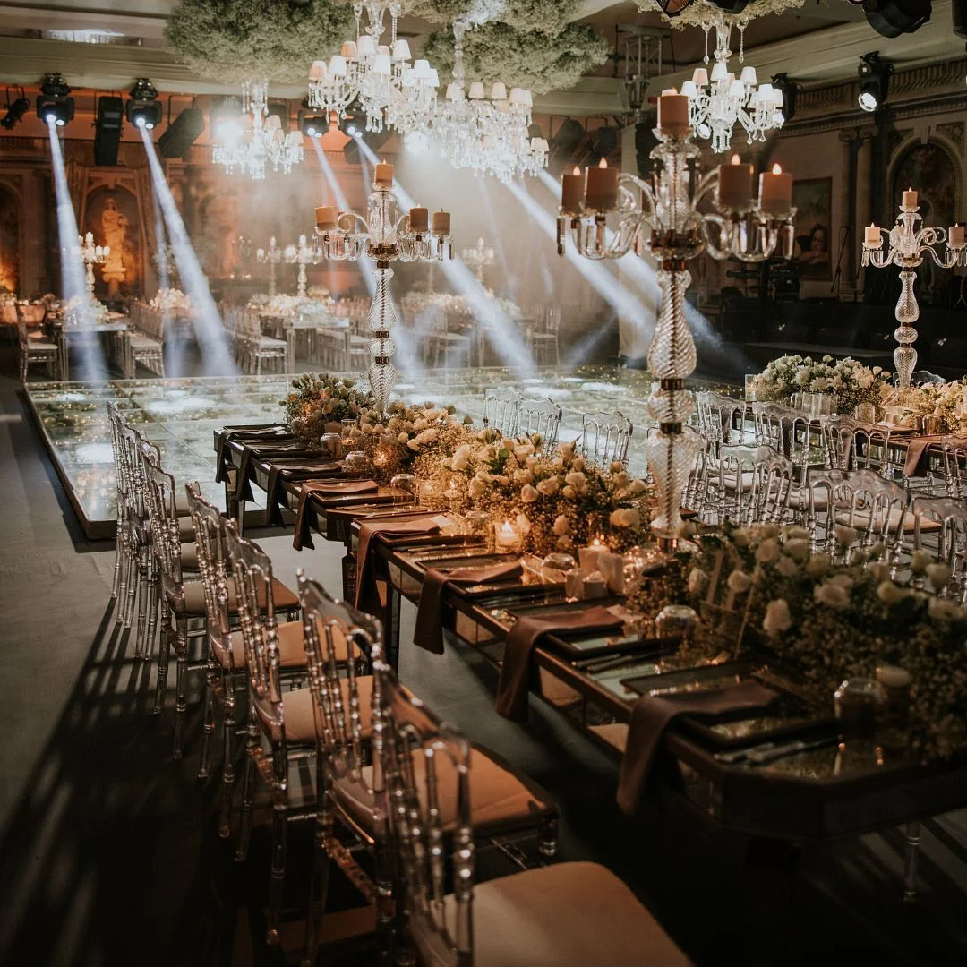 Long mirrored banquet table beneath crystal candelabras and stage light beams