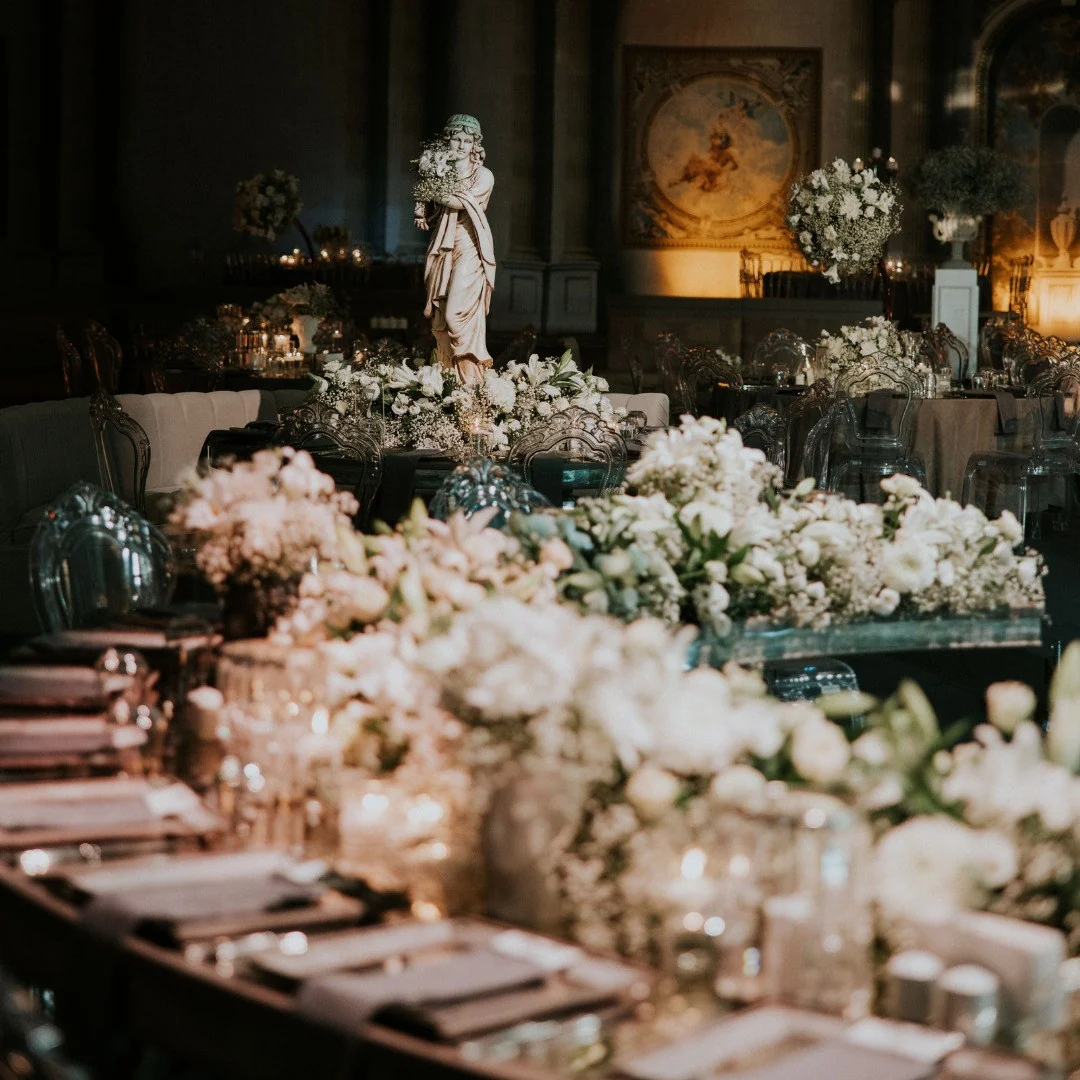 Long table dressed with white flowers, candles and a statue in low light