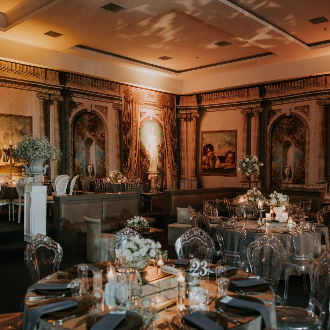 Round tables with clear chairs and lounge seating in a fresco-walled hall