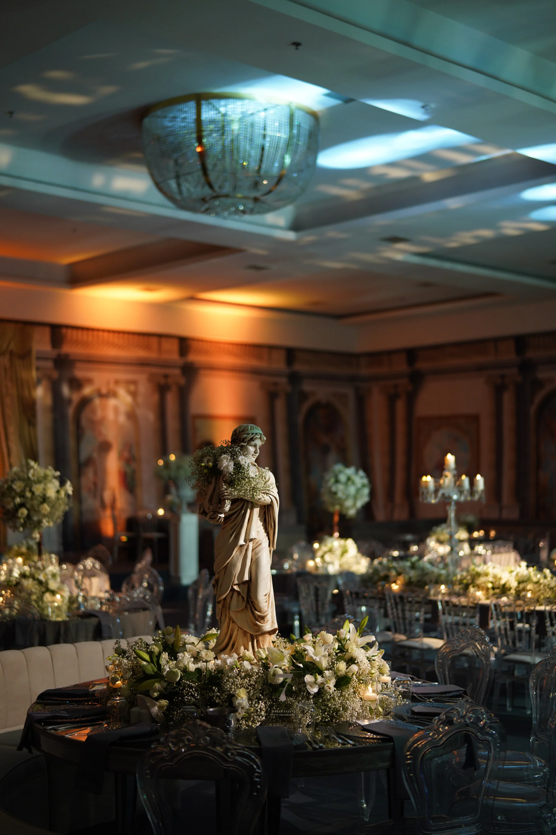 Round table with a statue ringed by white flowers beneath a crystal ceiling light