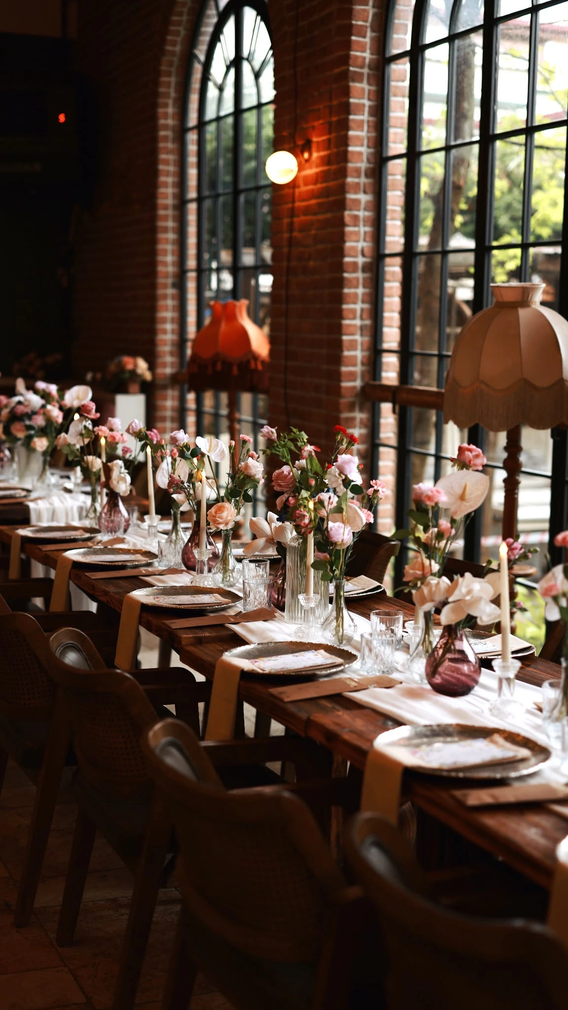 Wooden table with pink flowers running along black-framed arched windows in a brick-walled hall