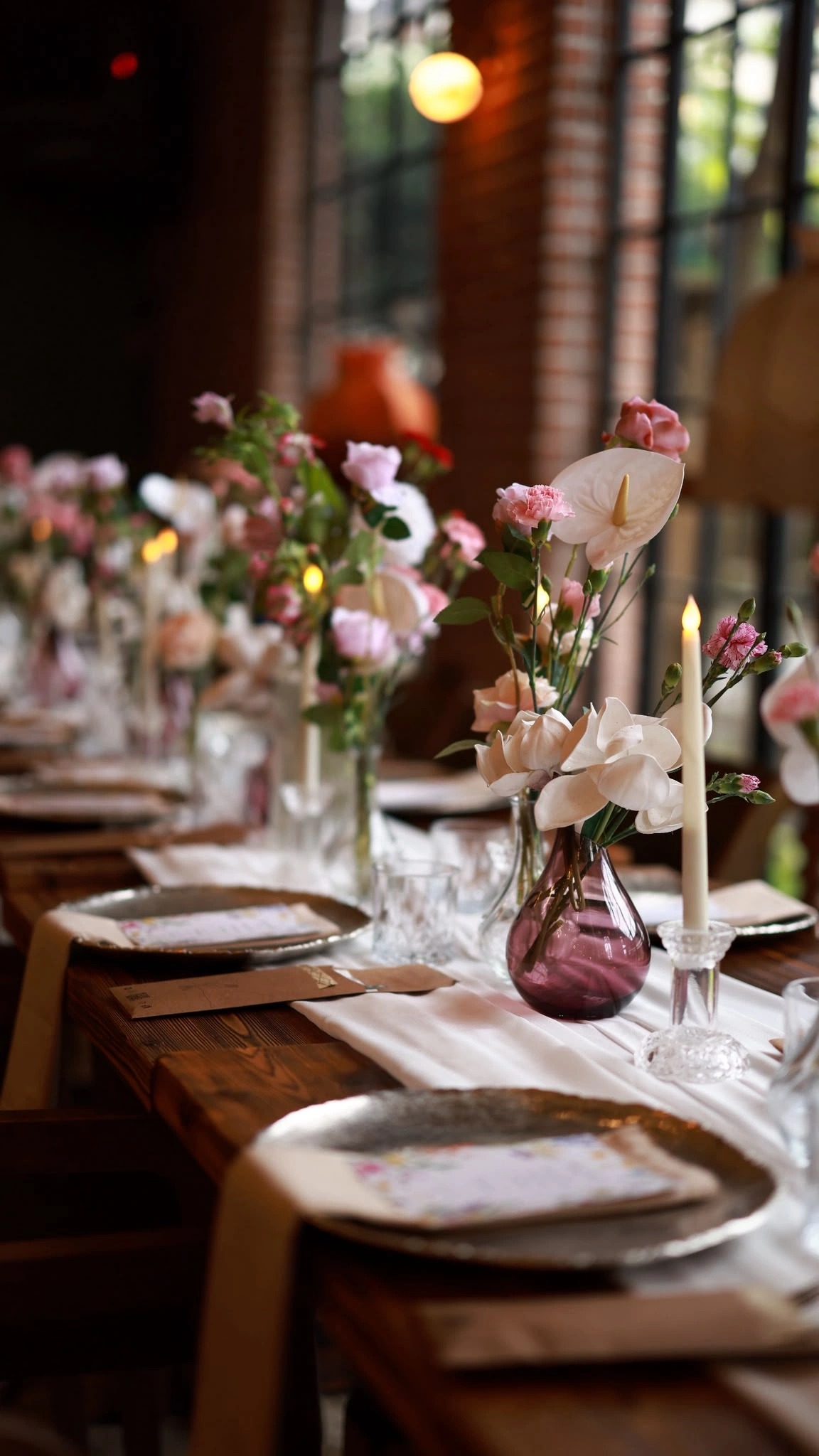 Table detail with pink roses, white anthurium and a taper candle in a plum glass vase