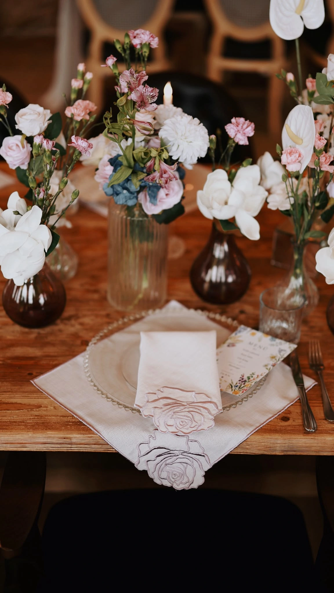 Overhead view of a rose-embroidered napkin, beaded-rim plate and vases of white and pink flowers