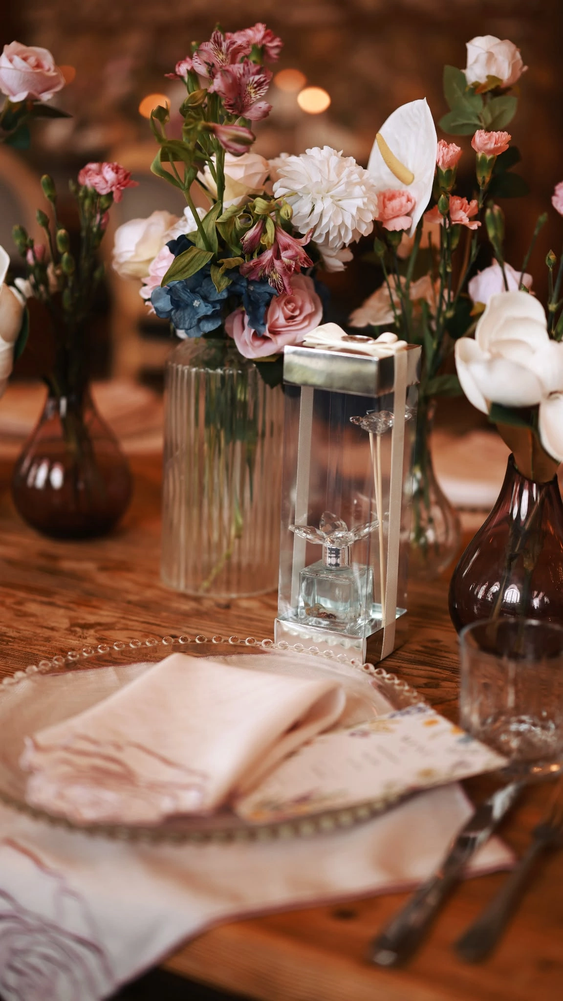 Napkin on a beaded-rim plate beside a clear acrylic block and pink roses with blue hydrangea