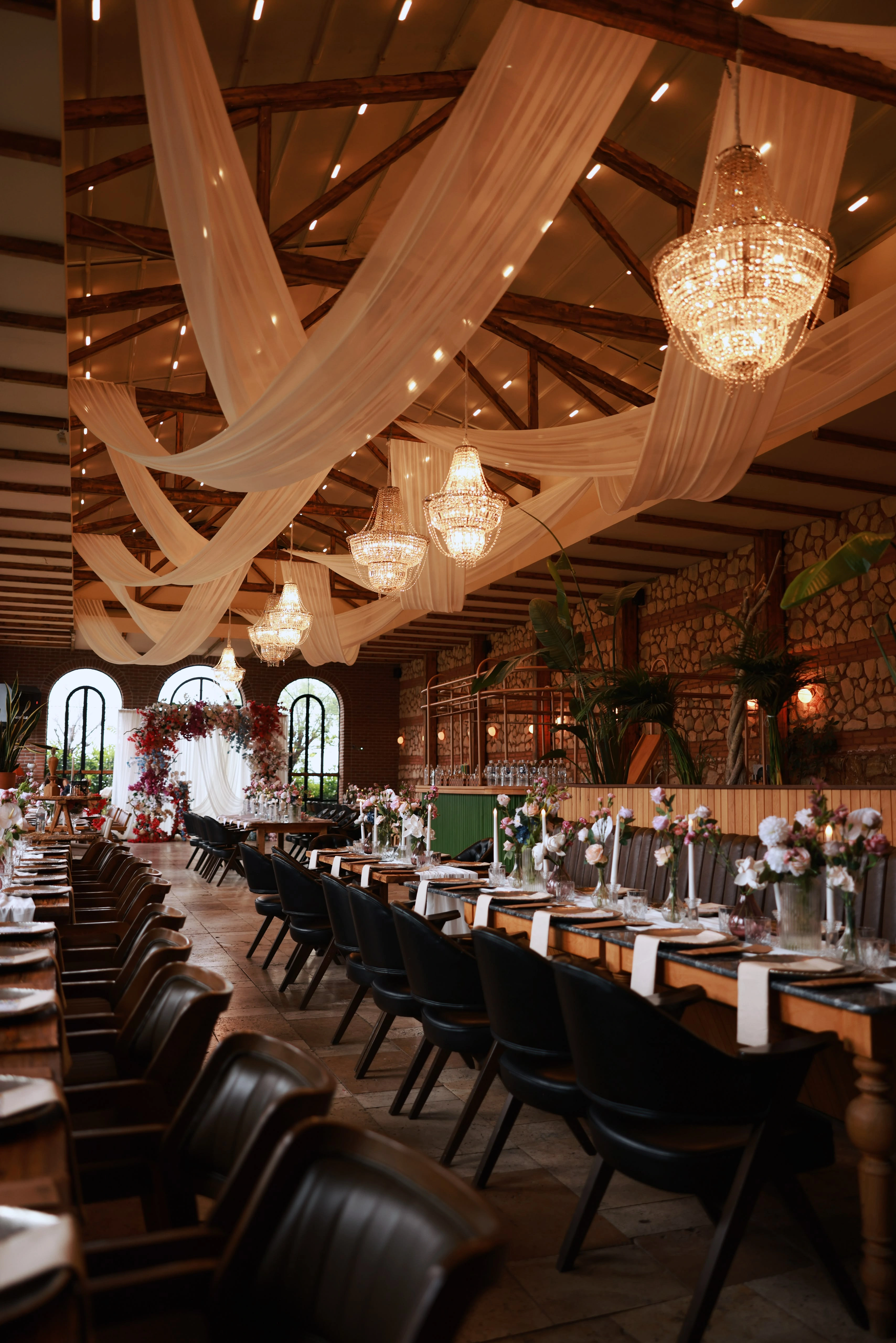 Wide-angle view of the hall with crisscrossing ceiling drapes, crystal chandeliers and a distant floral arch
