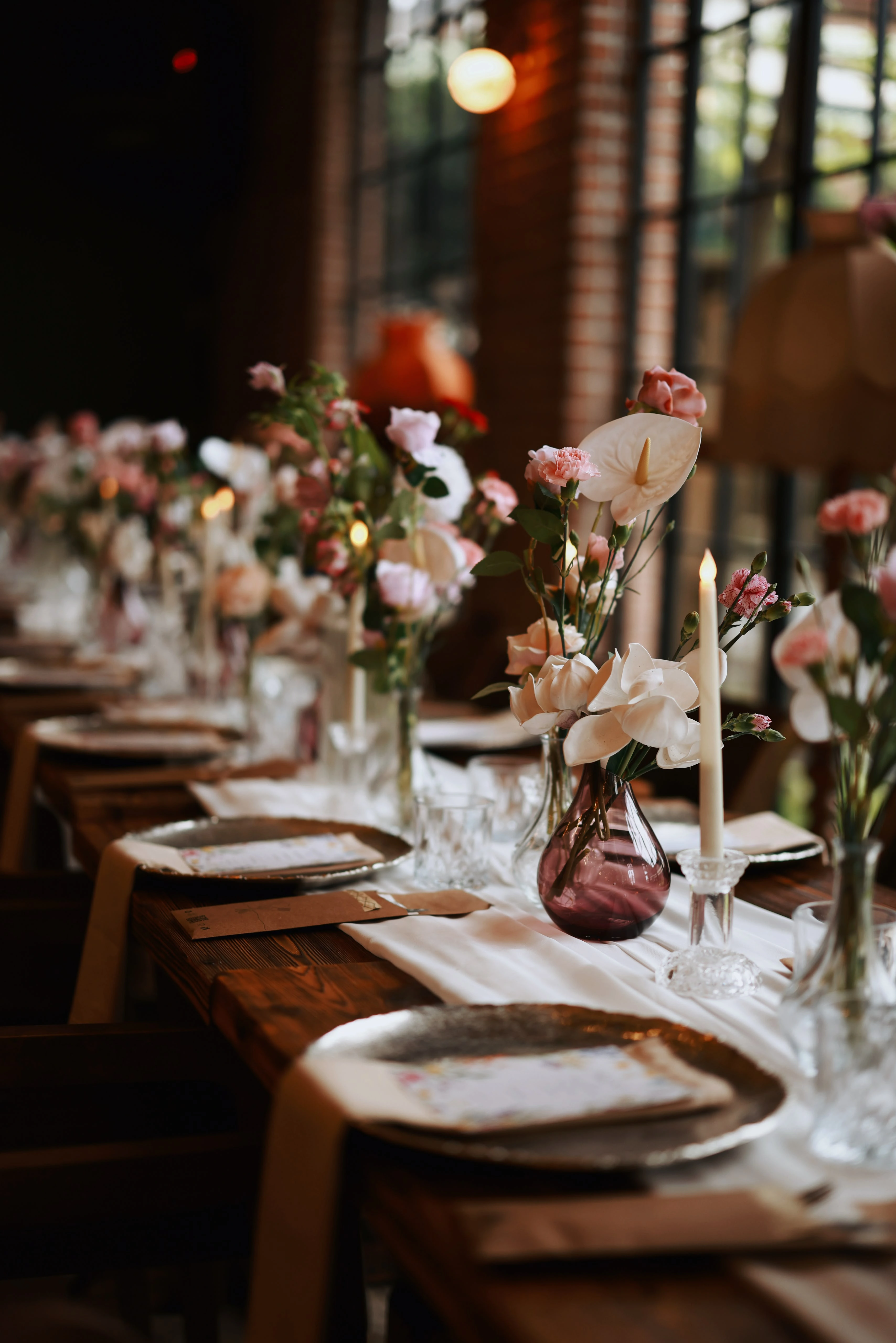 Row of tables with candles and pink flowers blurring toward red lampshades