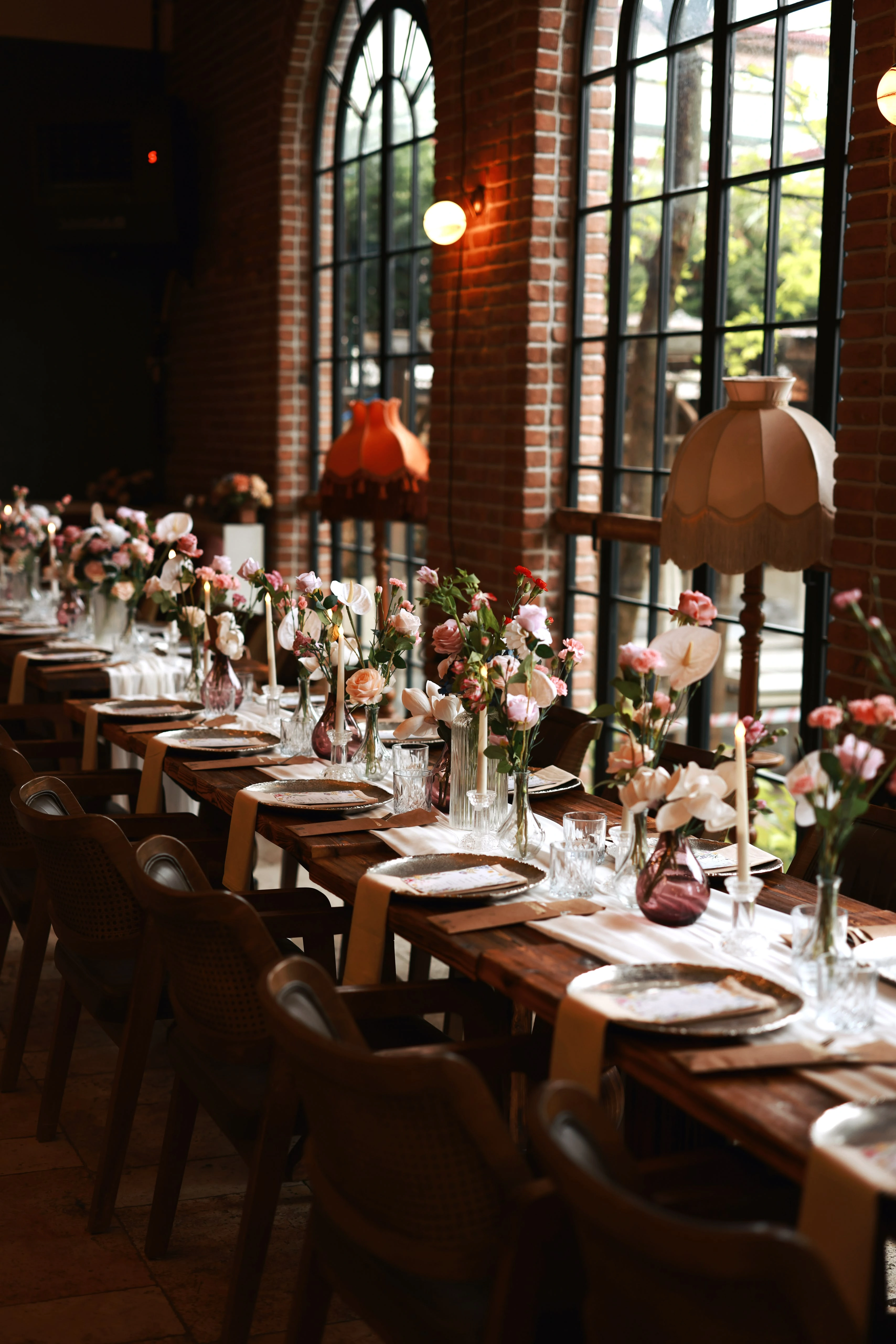 Flower-dressed table with wooden chairs lined along arched windows and a fringed floor lamp