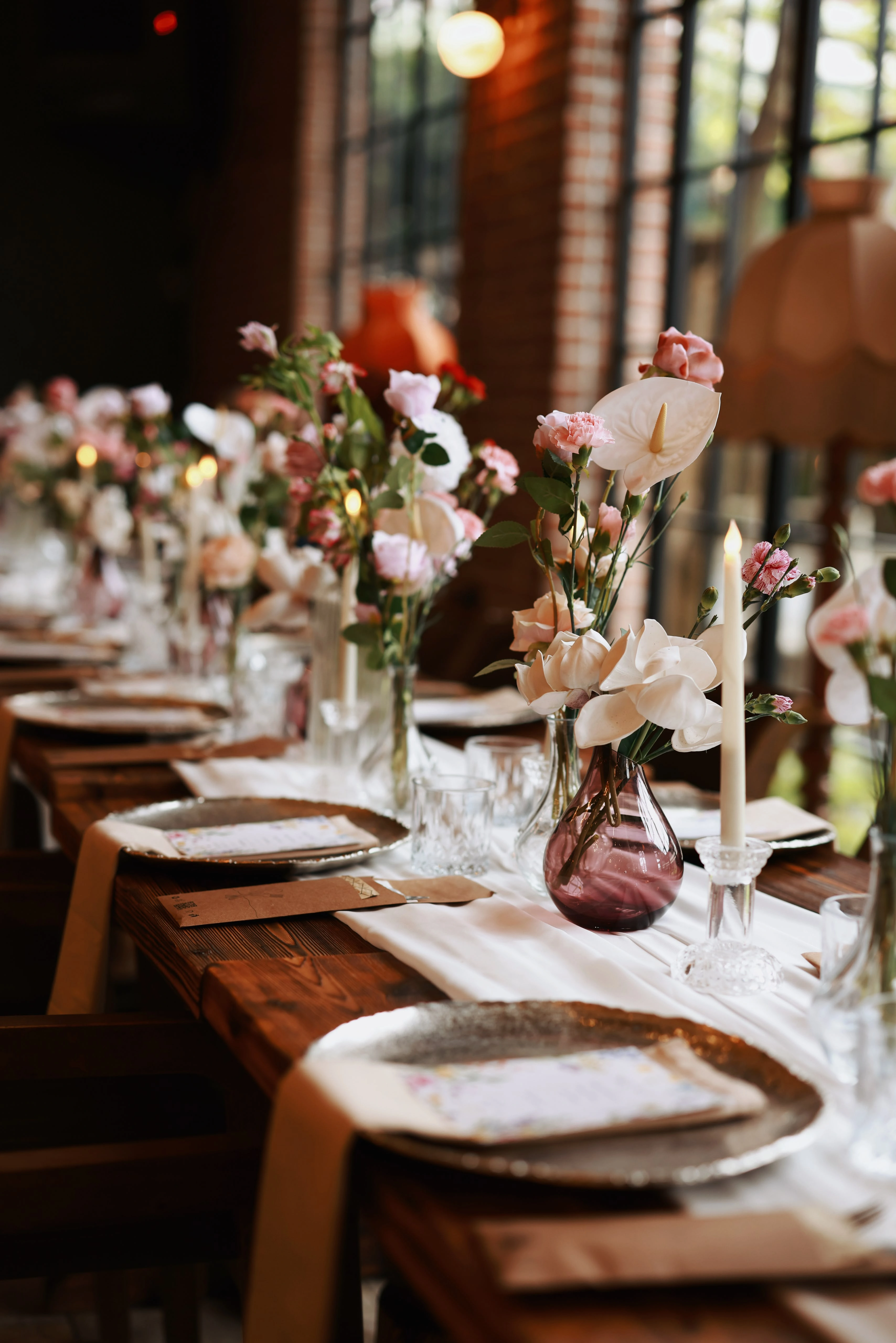 Low-angle view of a wooden table with menu cards on silver chargers, beige napkins and glass vases