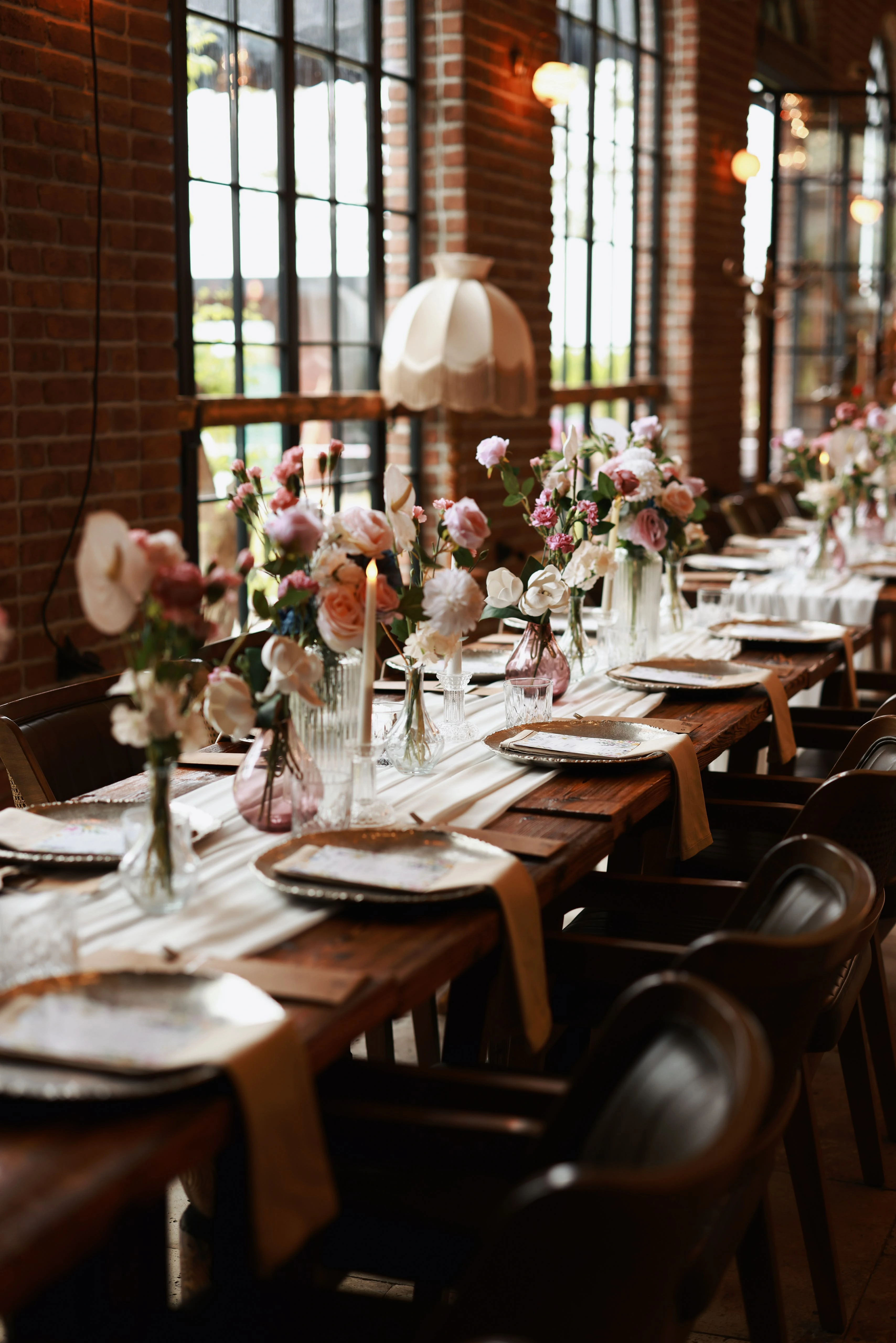 Flower-dressed table beneath a cream lampshade along daylit windows