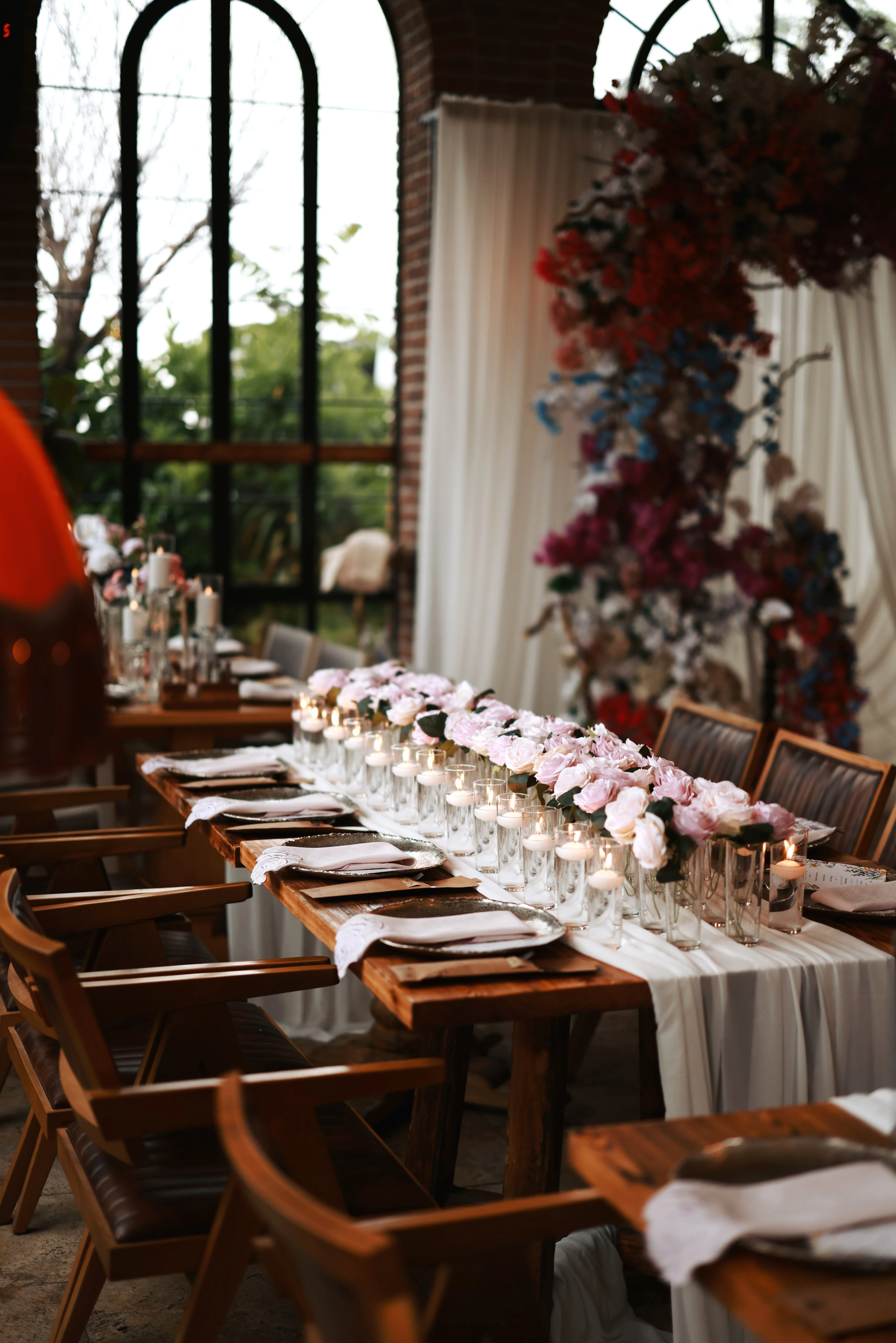 Side view of a candlelit pink rose runner extending from a window-side floral installation