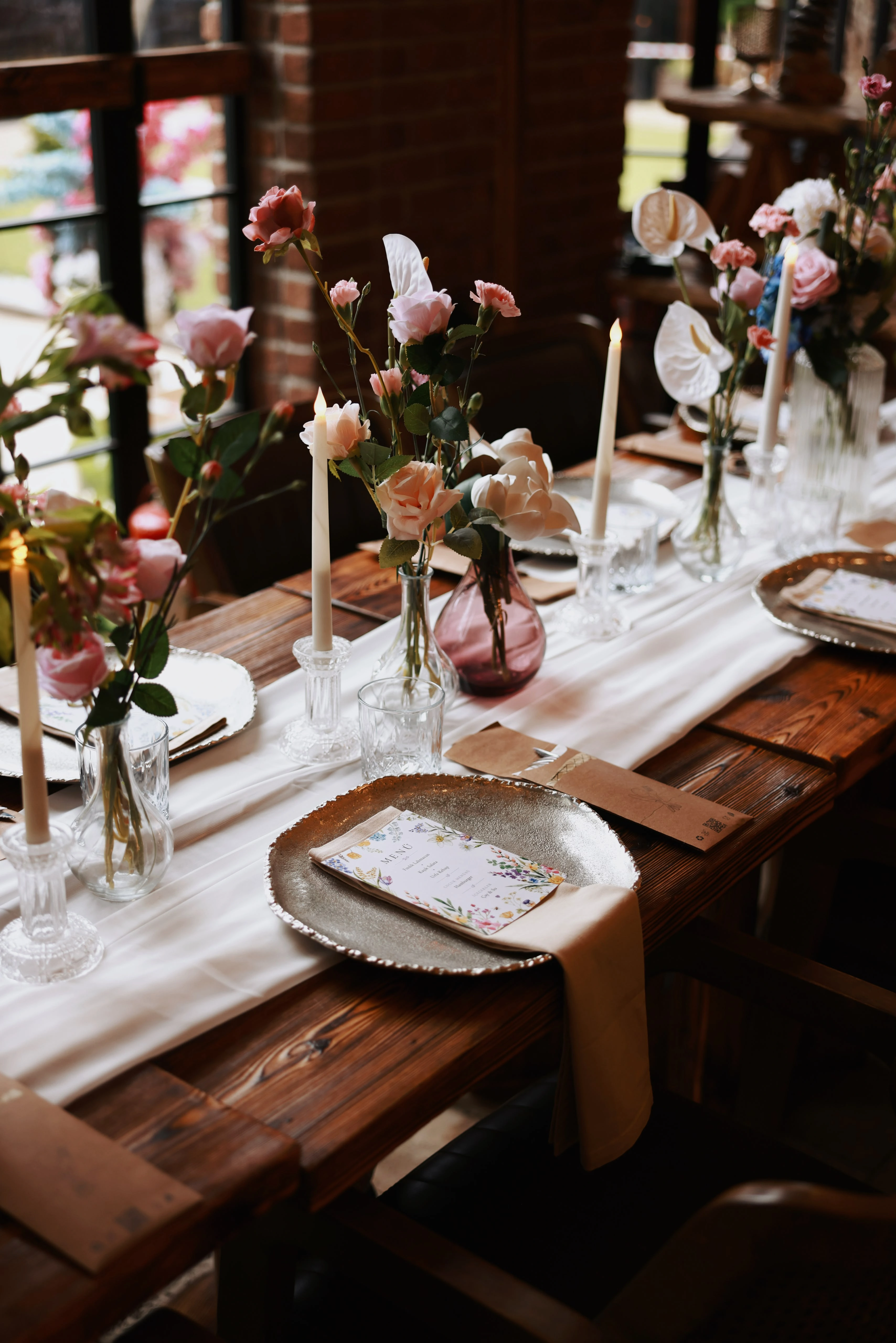 Angled top view of a wooden table with a white runner, taper candles and plates holding menu cards