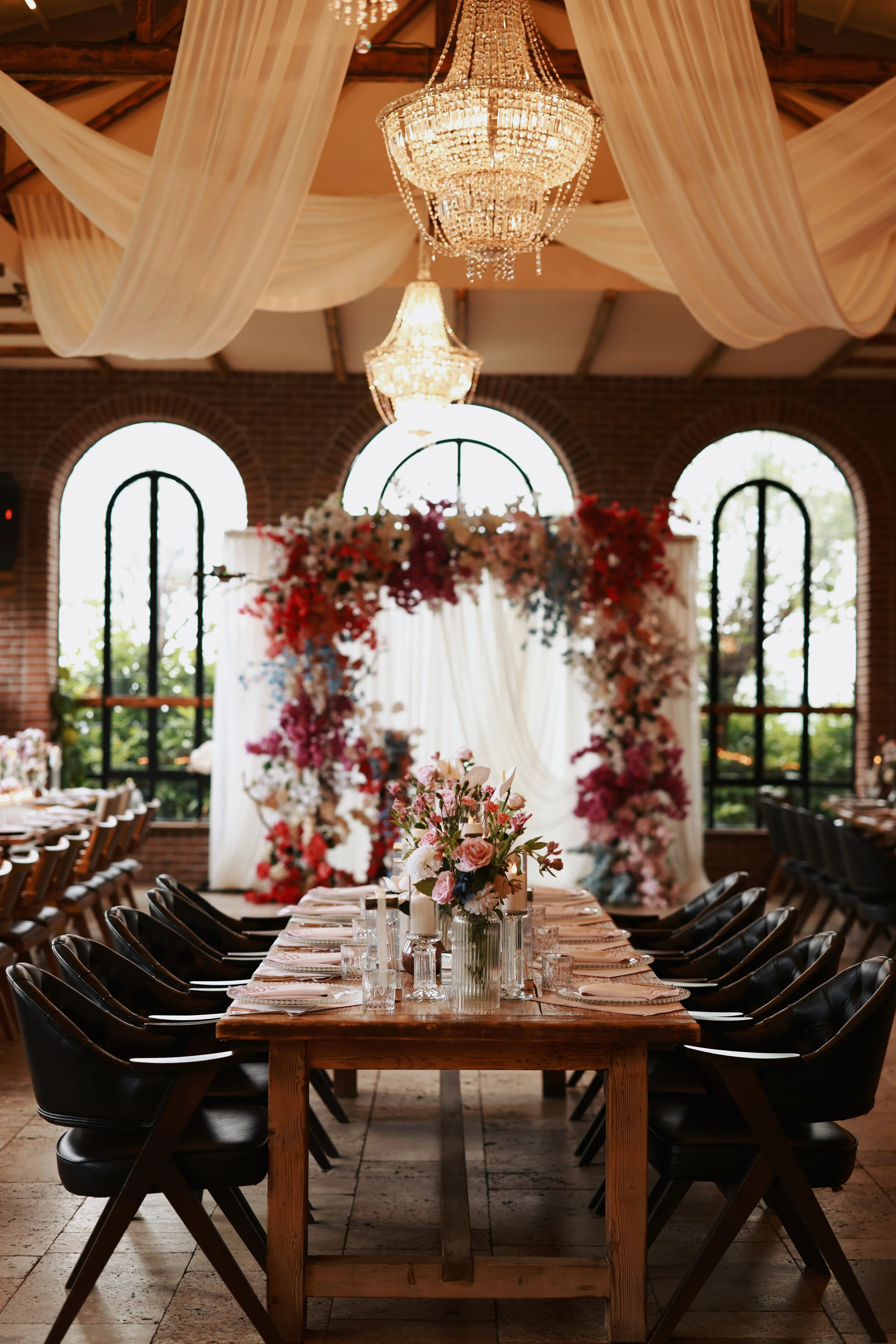 Engagement table leading to a floral arch in front of arched brick windows
