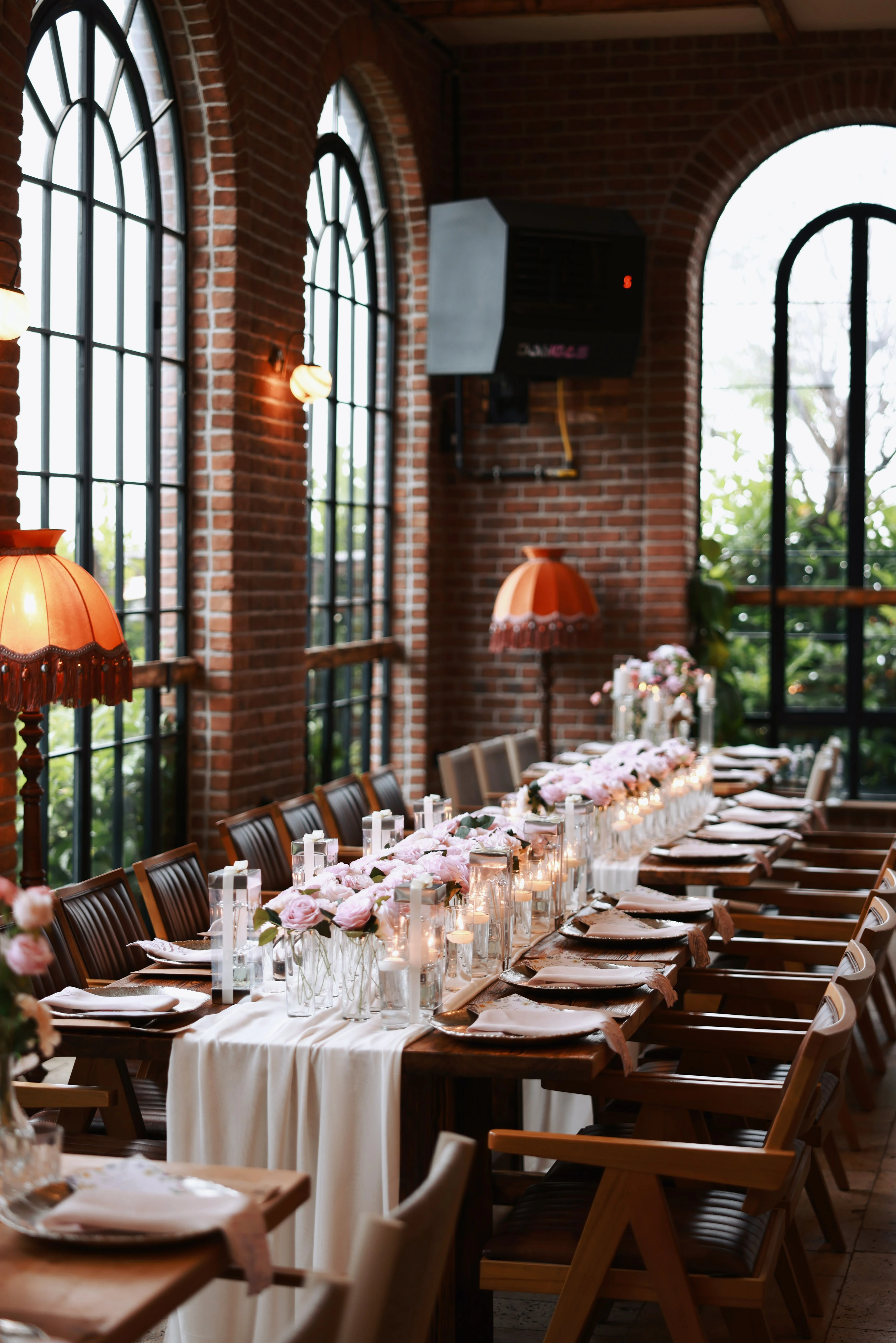 Long floral table in front of a brick wall and tall windows