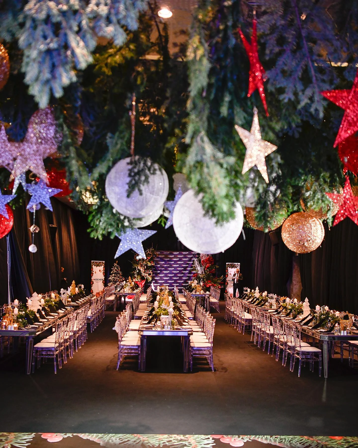 Hall with long tables beneath hanging pine branches, stars and white globes