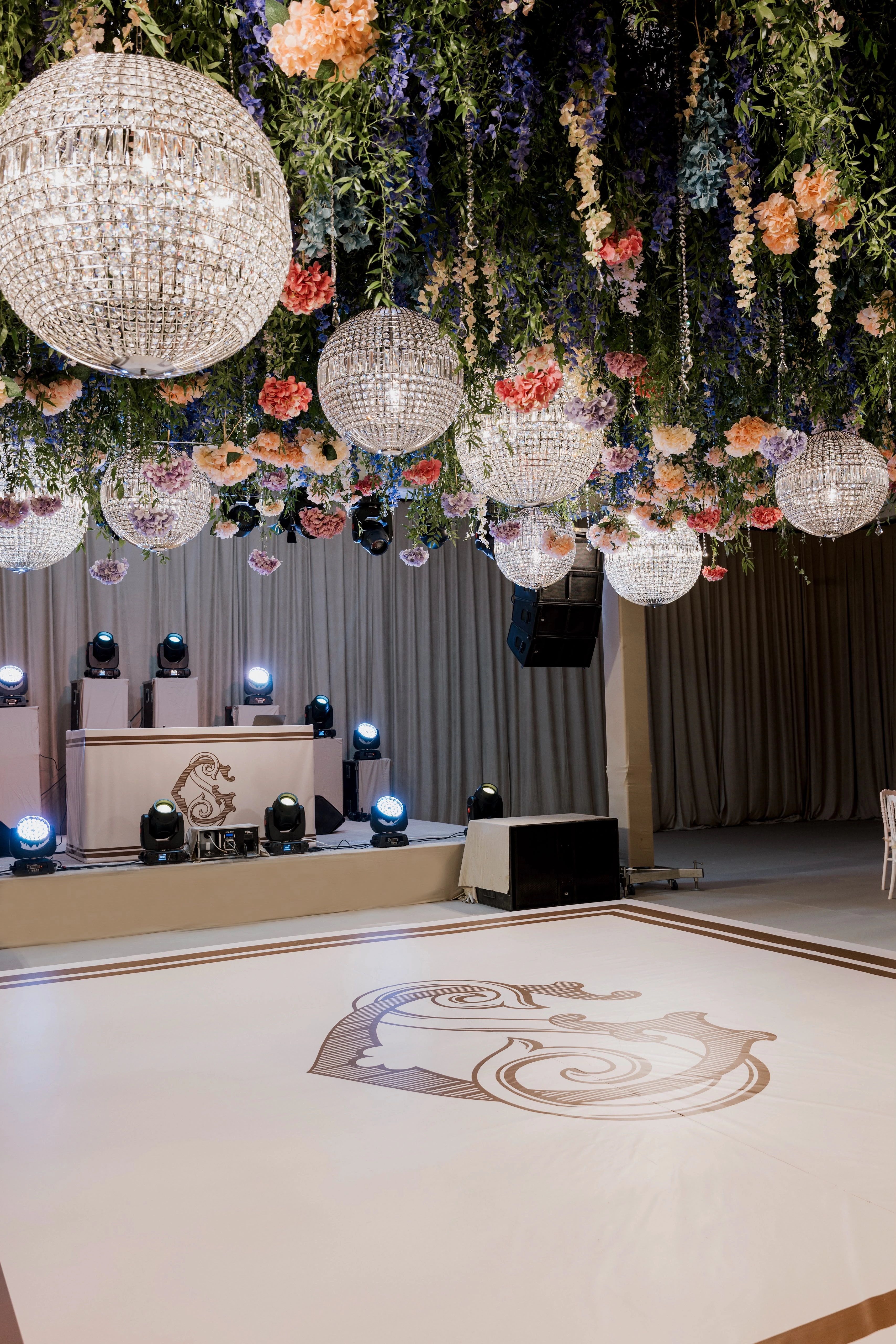 Monogrammed white dance floor and lit stage beneath crystal globe chandeliers and hanging flowers