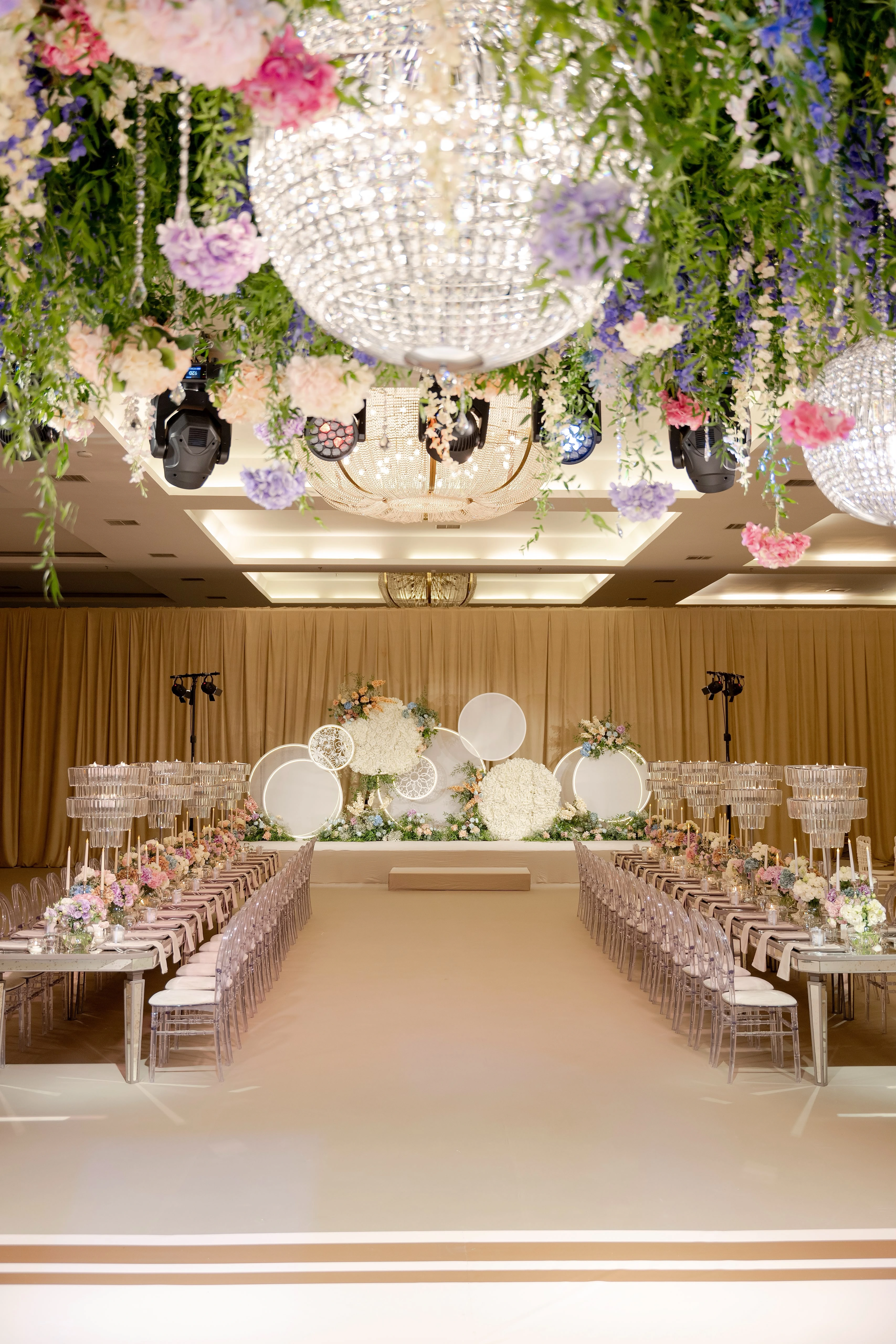 Aisle between two rows of long tables leading to a stage of white circular panels under a floral ceiling