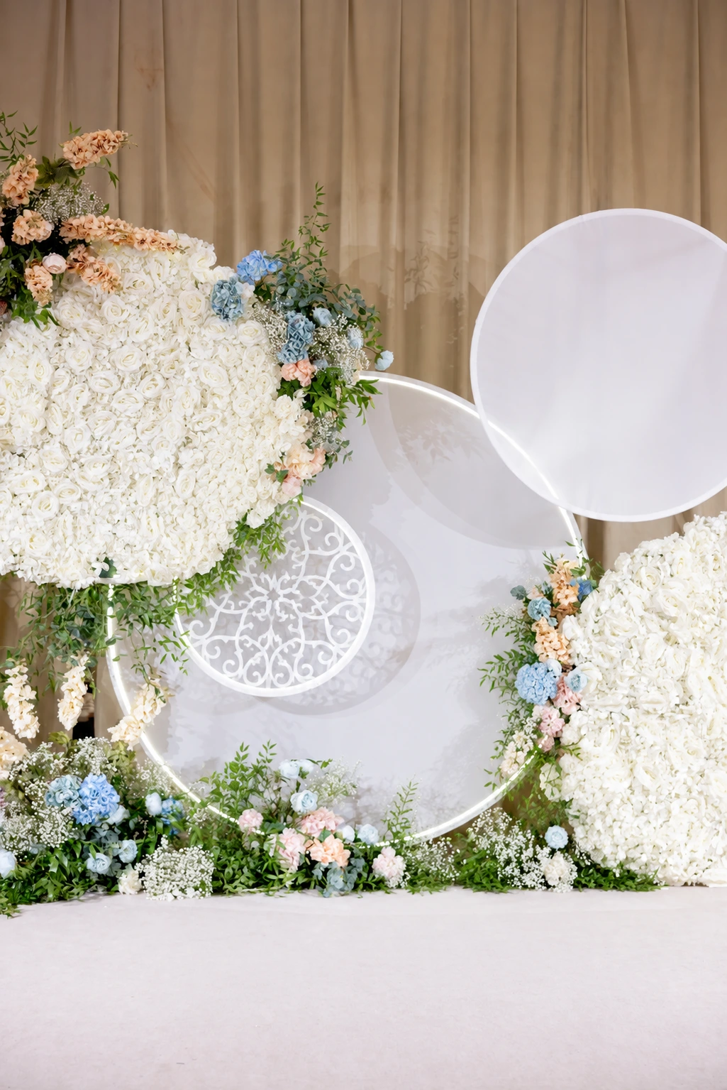 Stage backdrop of white hydrangea clusters, translucent lace-patterned circles and blue flowers