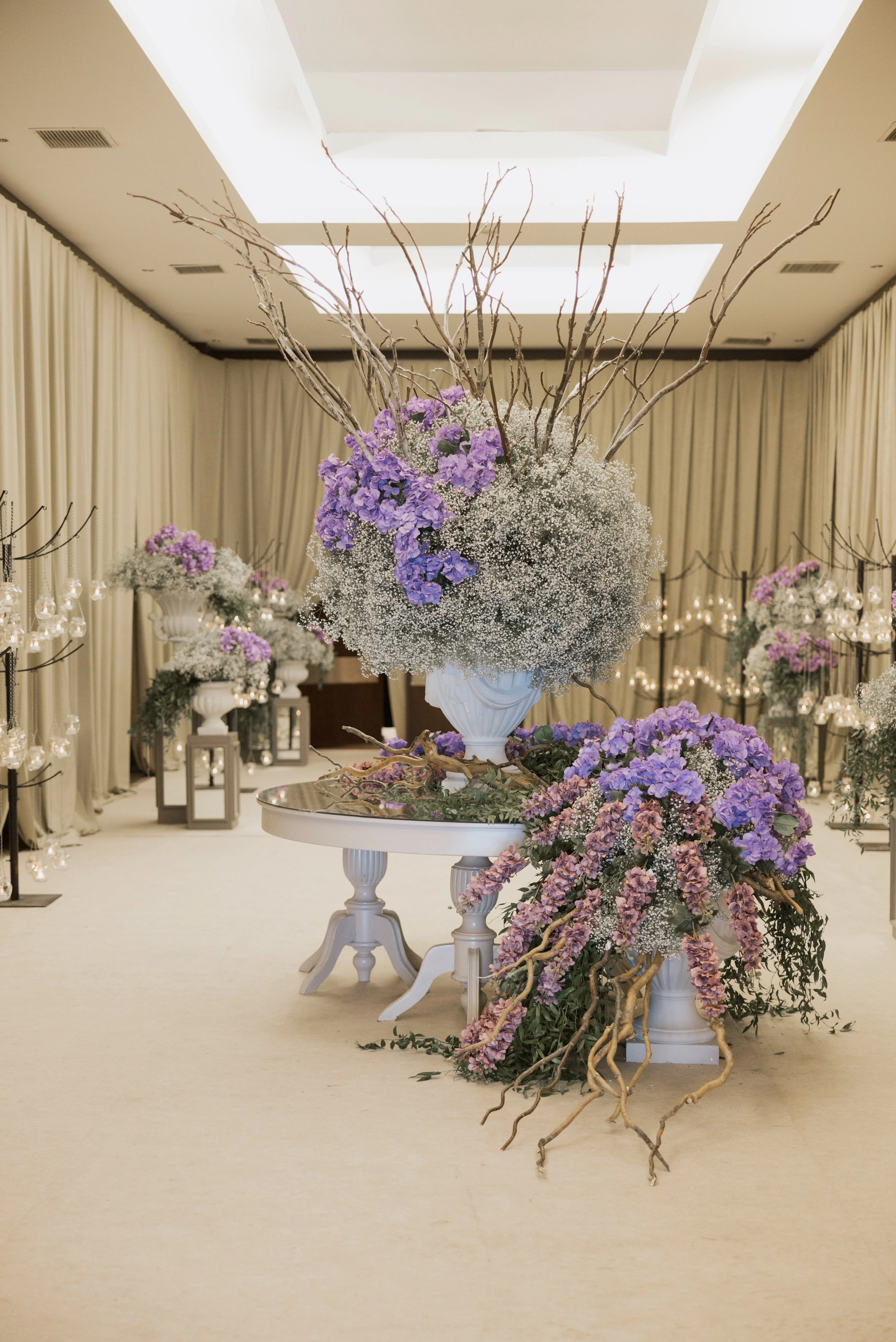 Large arrangement of purple hydrangea, baby's breath and branches on a white pedestal table