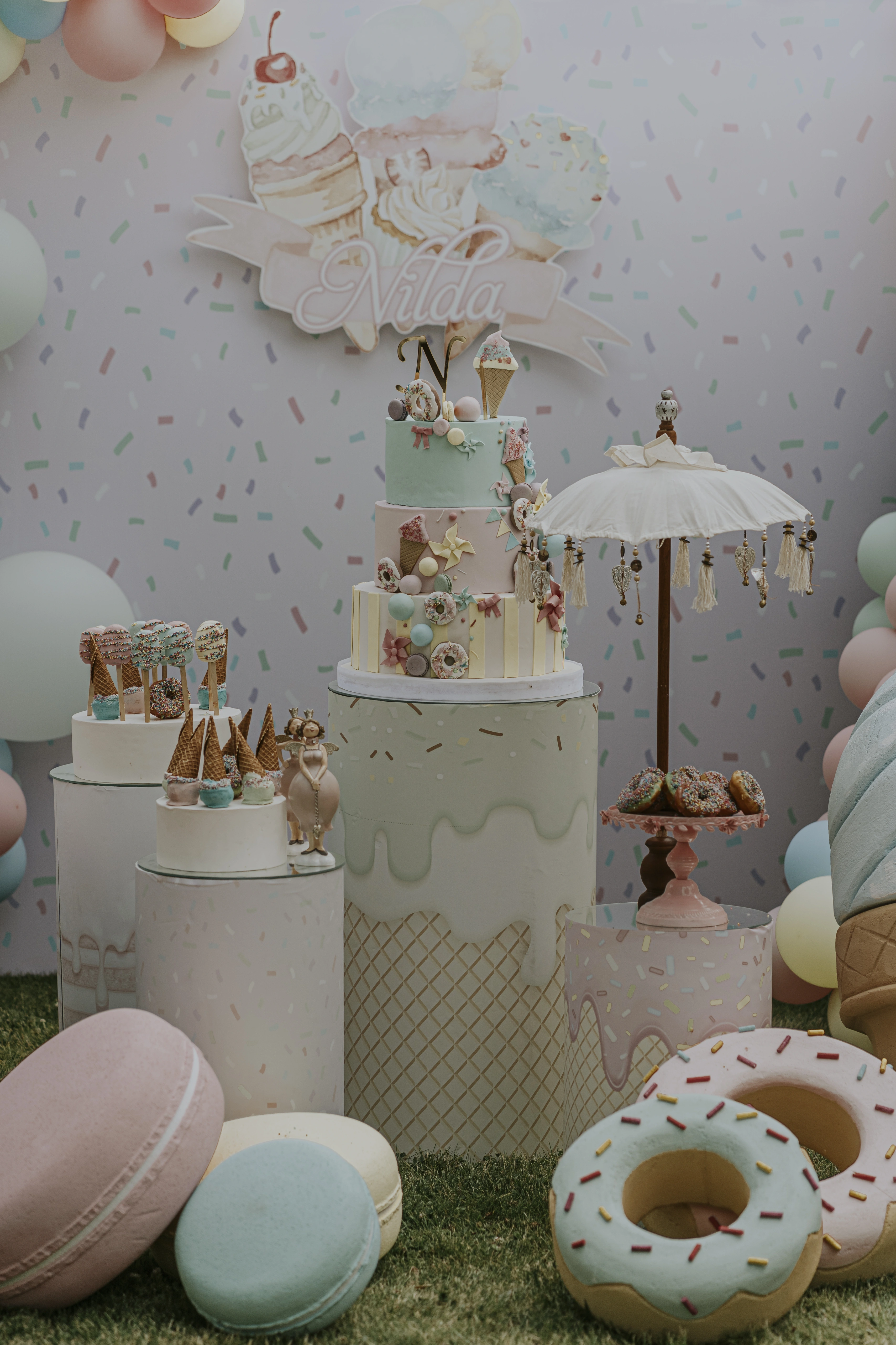 Dessert scene with a tiered cake, parasol, giant doughnuts and macarons