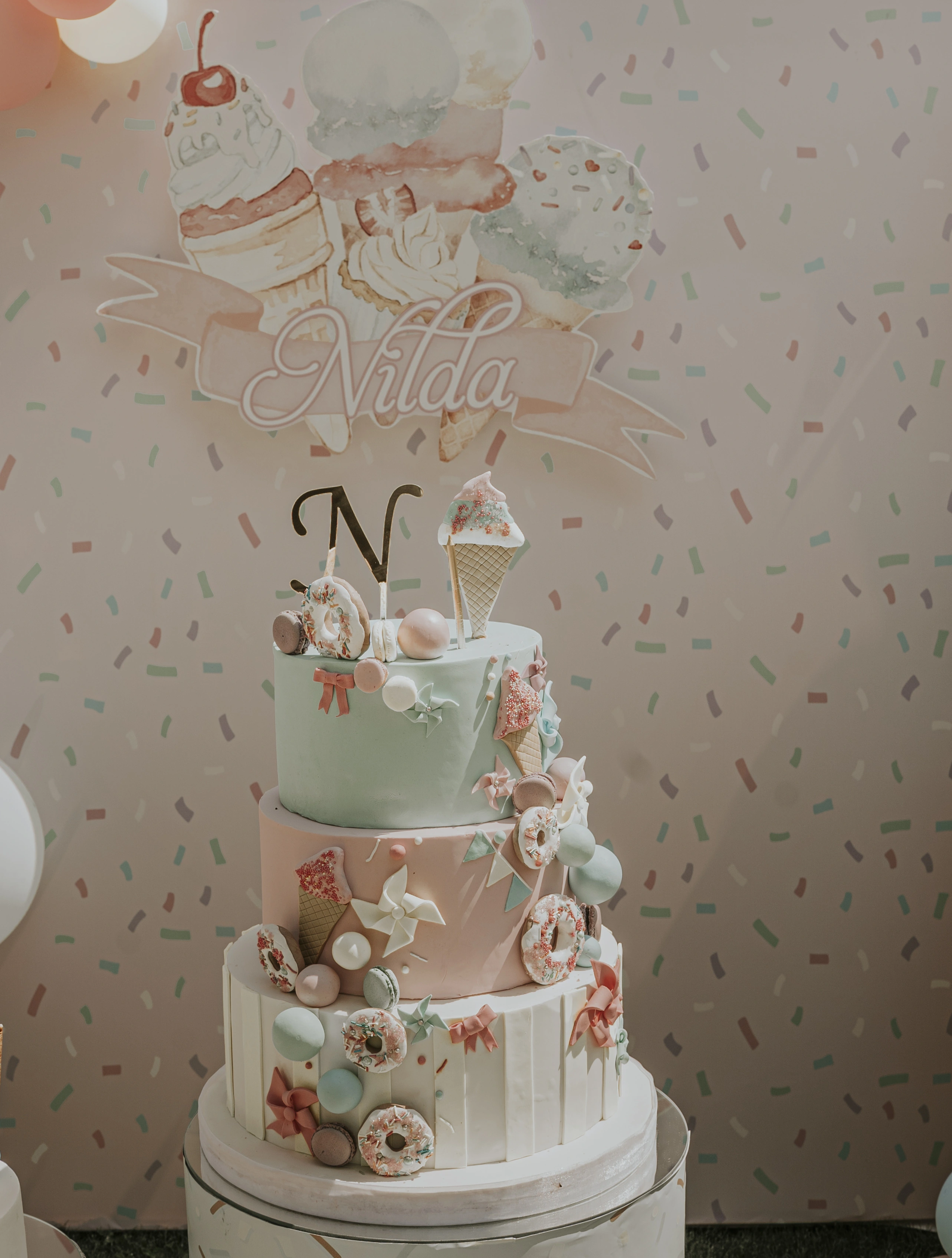 Three-tier pastel cake decorated with doughnuts, macarons and ice cream