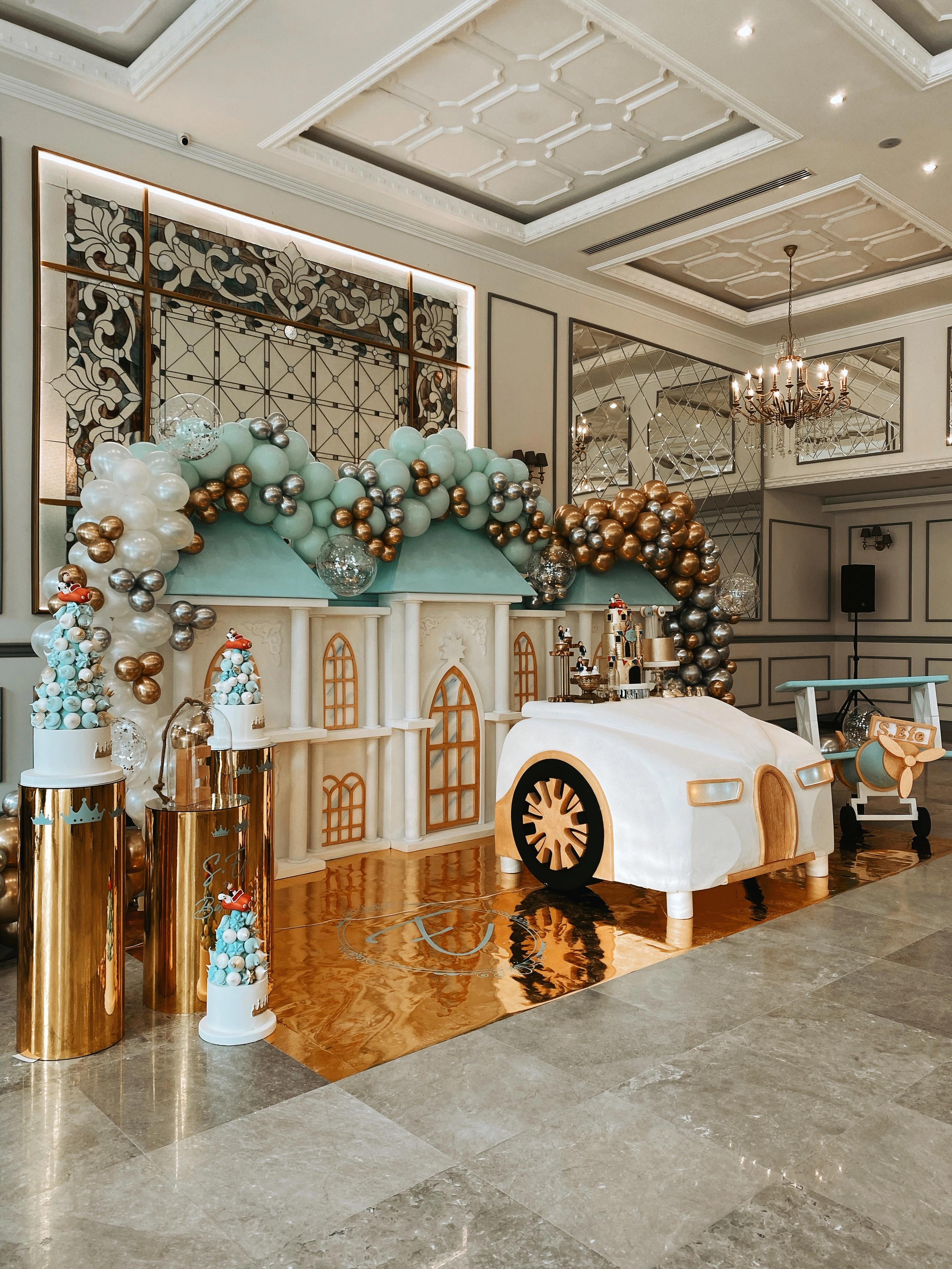 Salonun genel görünümü: mint ve altın balon kemeri, minyatür evler ve beyaz vintage otomobil