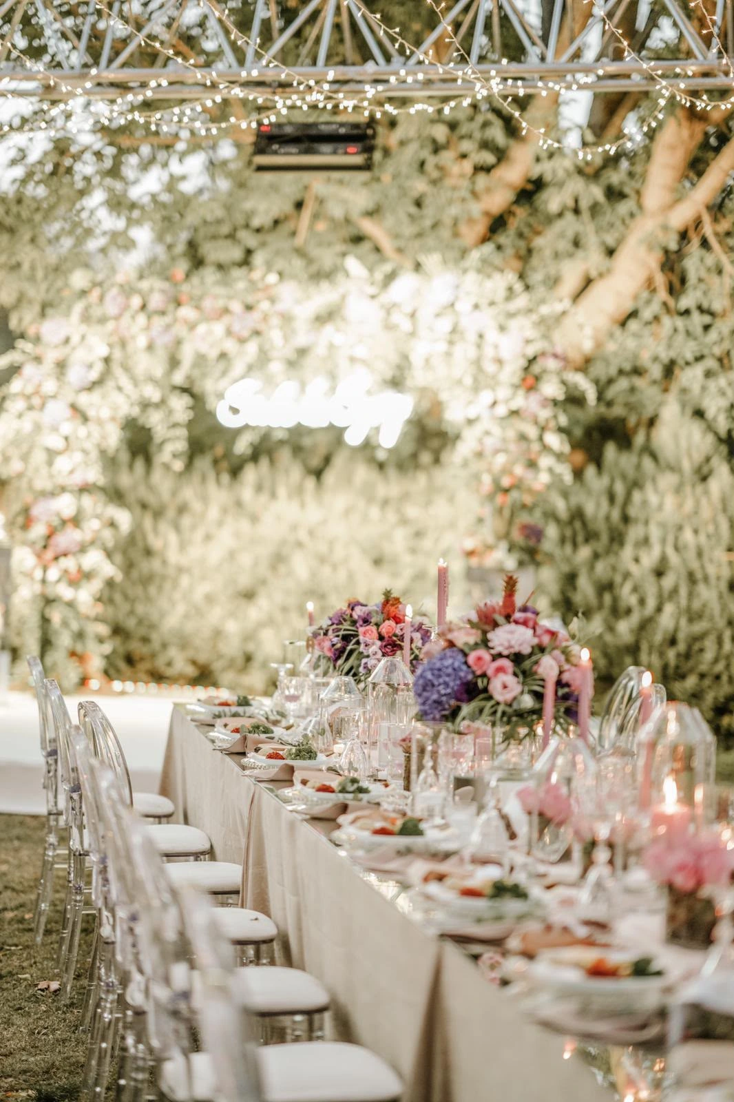 Vertical perspective of a long table leading to a glowing neon sign on a greenery wall