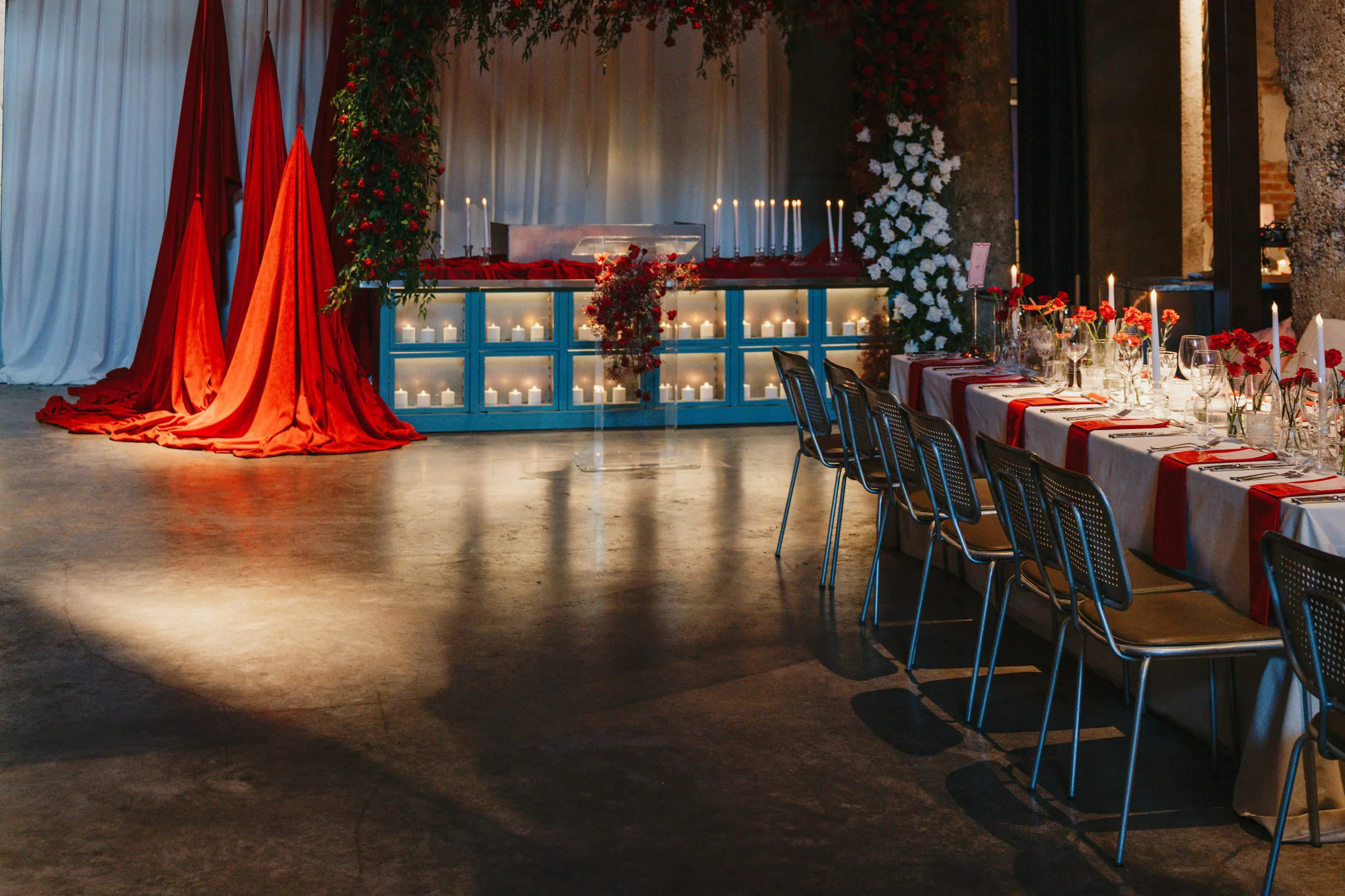 Stone-walled event space with red drapery, candles and a long table