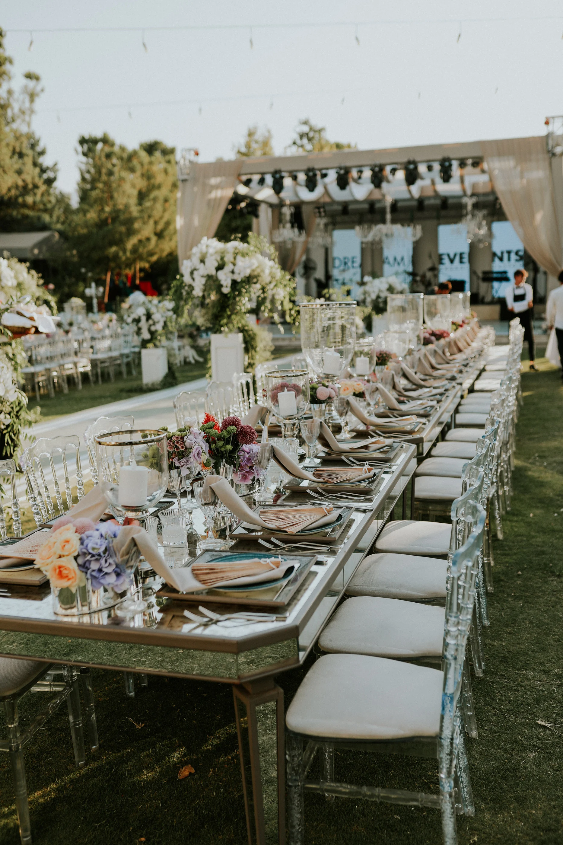 Mirrored long table with folded napkins and pastel flowers stretching toward the stage