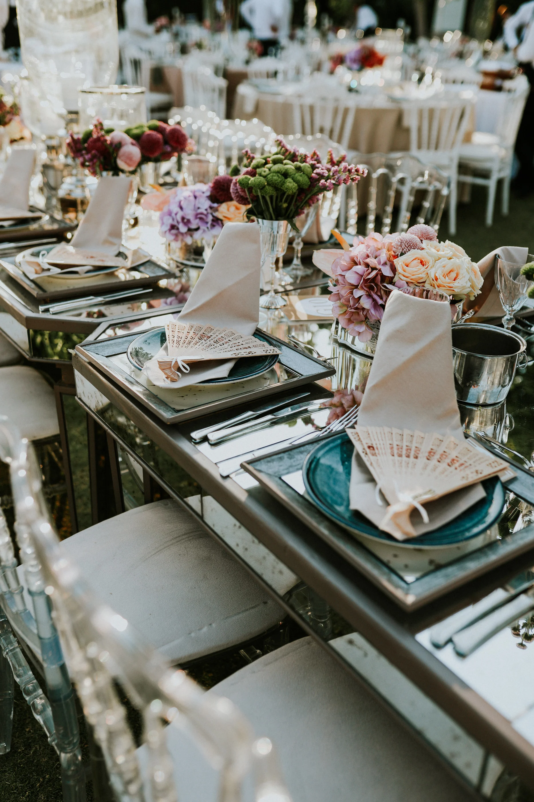 High-angle view of a turquoise plate, fan-folded napkin and colourful flowers on a mirrored table