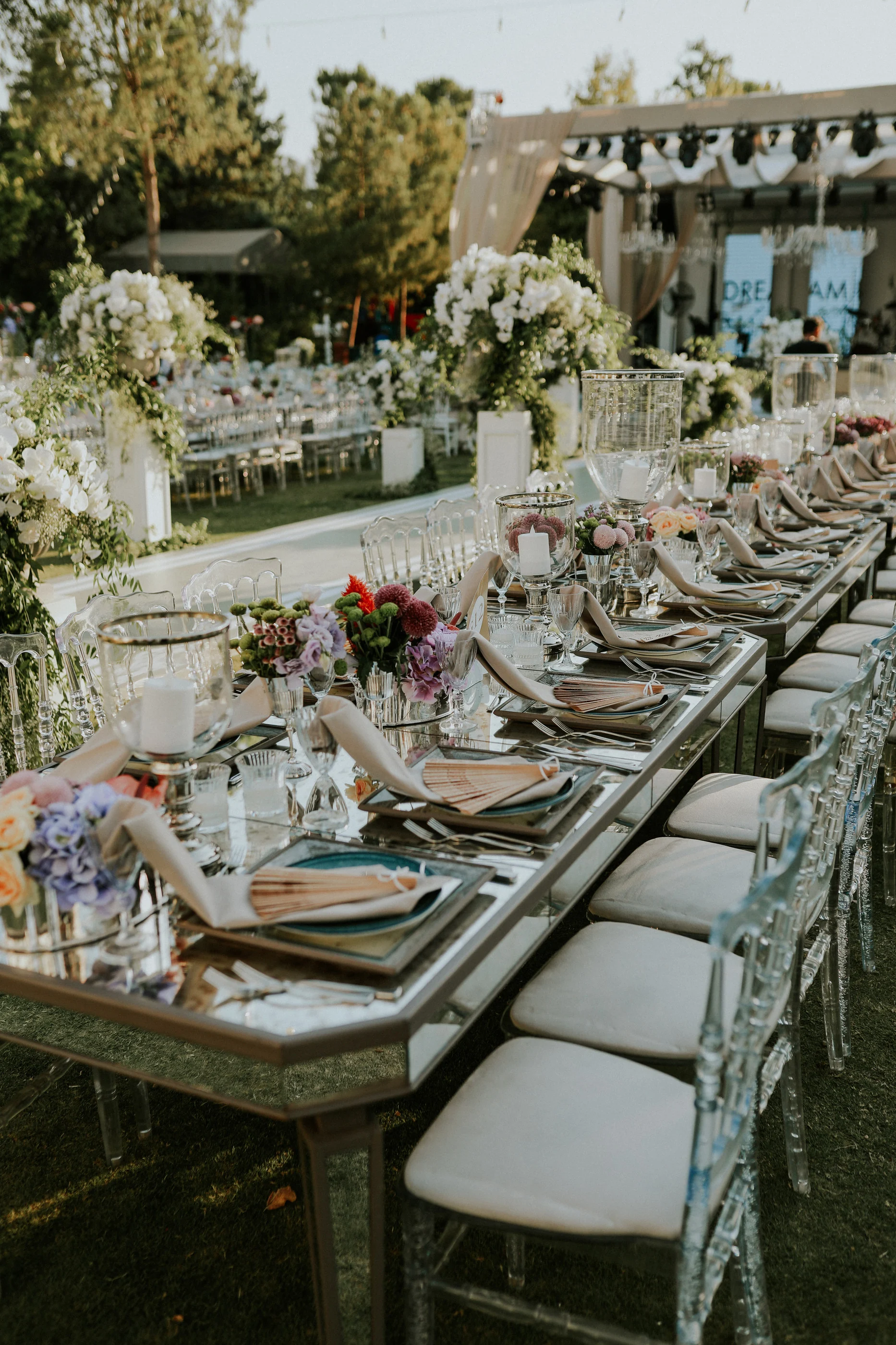 Diagonal view of a mirrored long table with white flower columns and the stage behind