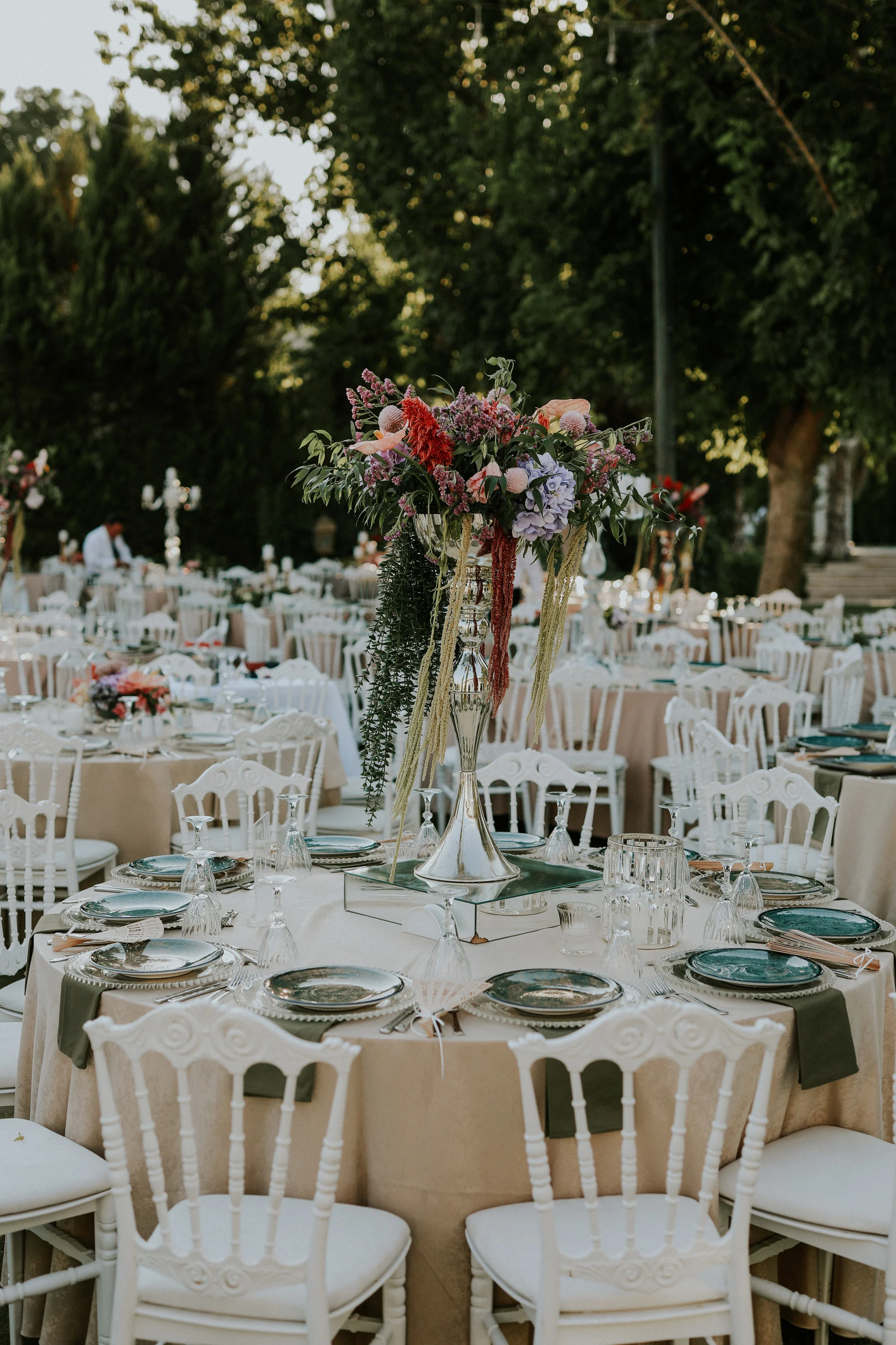 Tall red and purple floral arrangement on a beige round table with white chairs